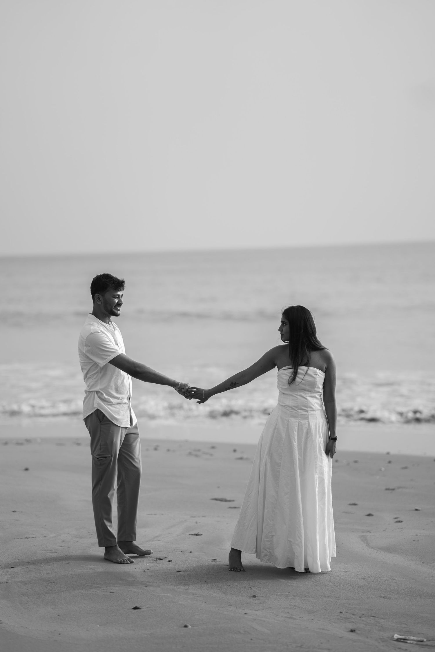 A romantic black and white sequence shows a couple holding hands and walking together on a sandy beach.