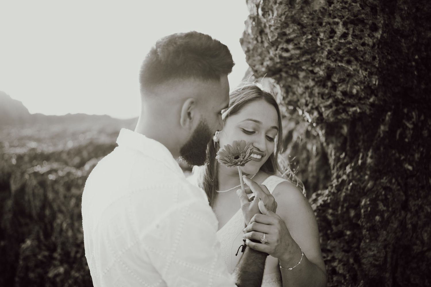 A romantic black and white moment shared between a couple drinking from glass bottles in nature.