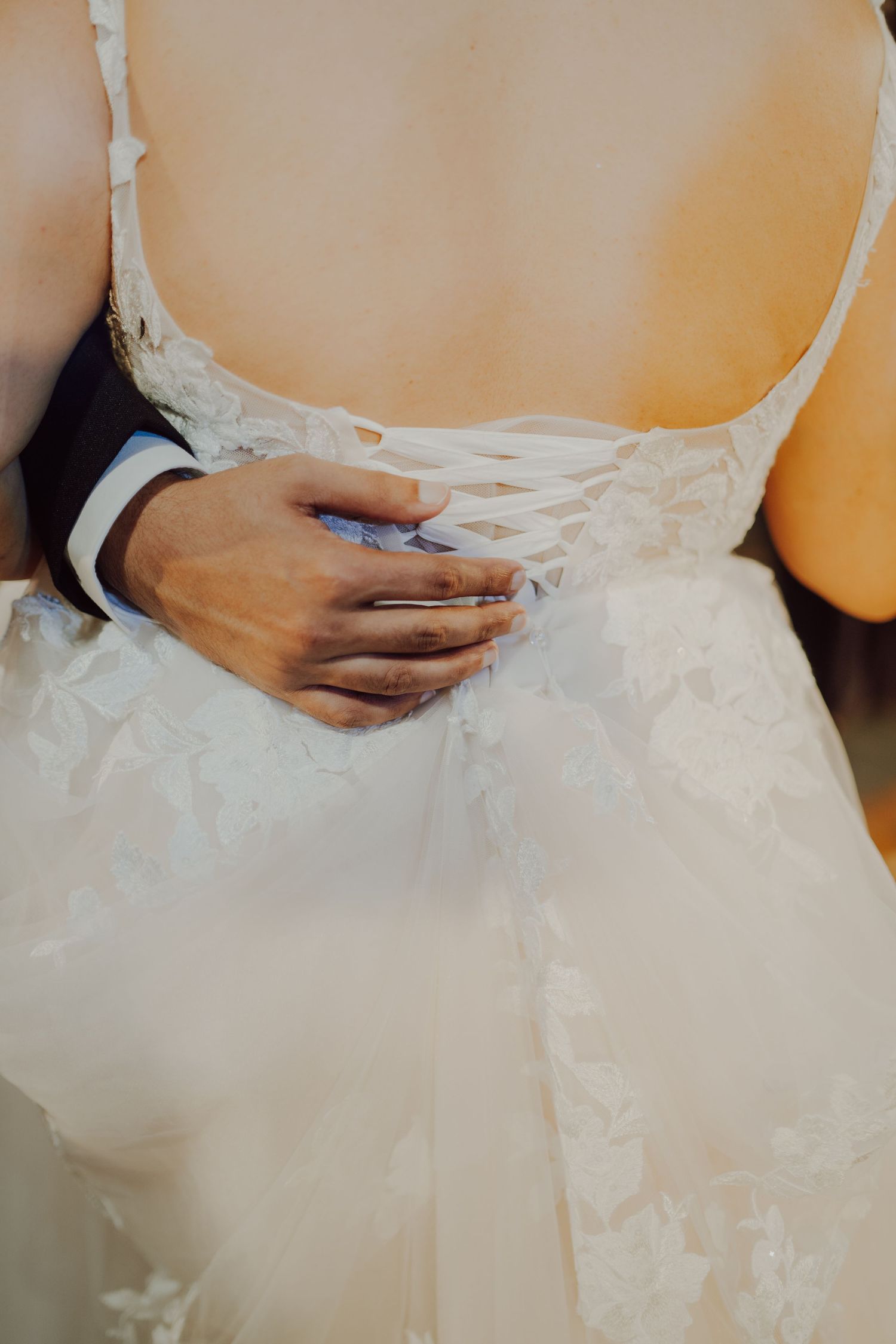 Close-up of hands embracing around a white lace wedding dress.