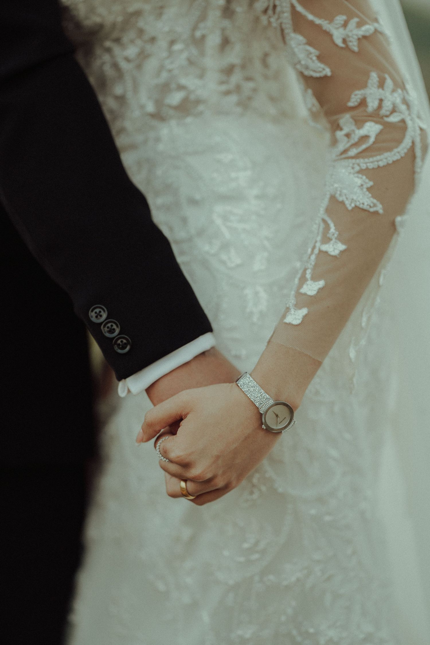 Close-up of couple holding hands showing detailed lace sleeve and wristwatch.