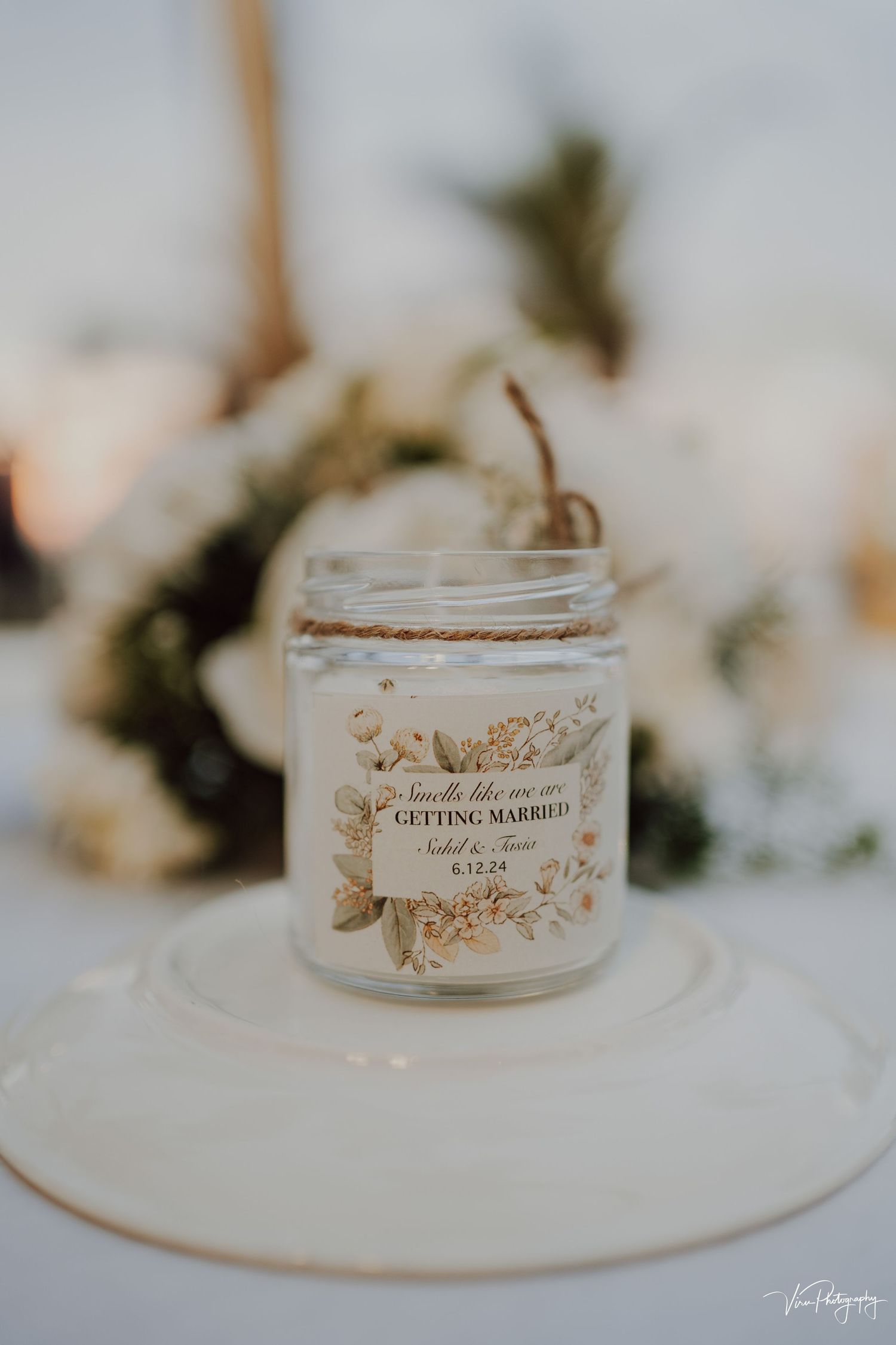 A decorative wedding candle in a mason jar with floral design and 'Getting Married' text sits on a white surface.