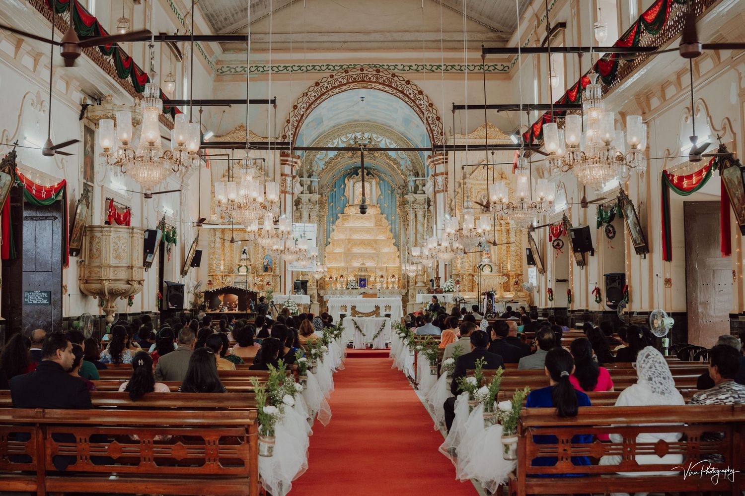 Church wedding ceremony with ornate decorations, chandeliers, and red carpet in a traditional cathedral setting.