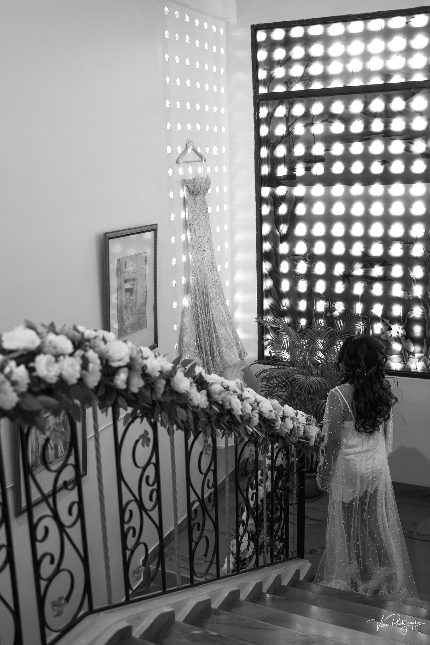 Elegant staircase decorated with floral arrangements and ornate railings casting dramatic shadows through window screens.
