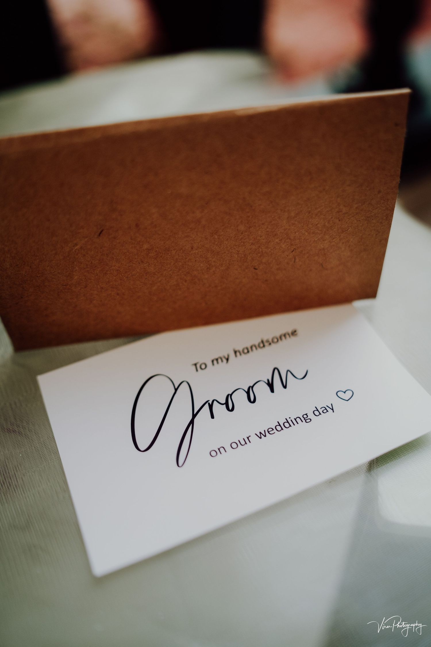 A close-up shot of a white wedding card with handwritten text 'To my handsome groom on our wedding day' and a heart.