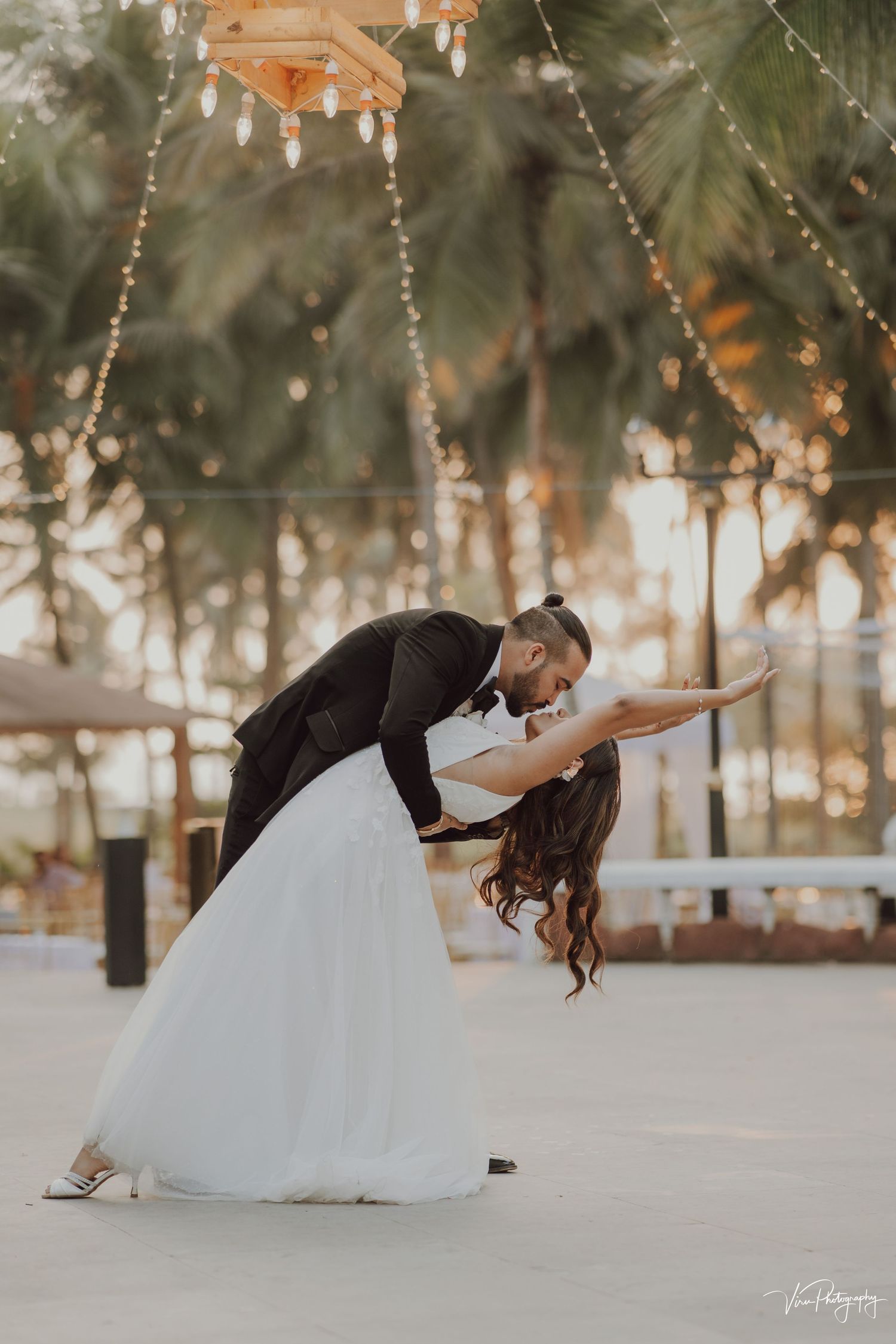 A couple dances gracefully outdoors at their wedding, with the bride in a white tulle gown and groom in black suit.