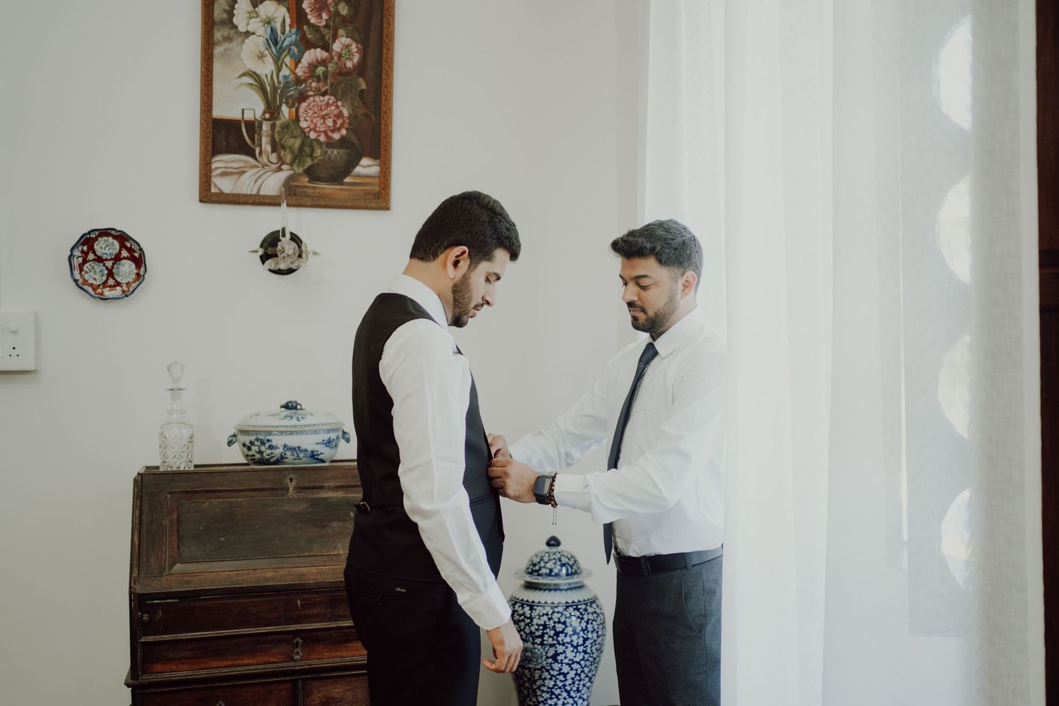Two people in formal wear preparing for an event near a vintage dresser.