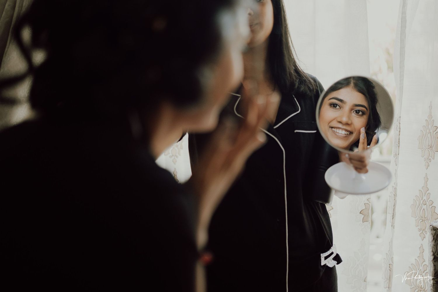 Person in black coat smiles while looking at their reflection in a mirror.