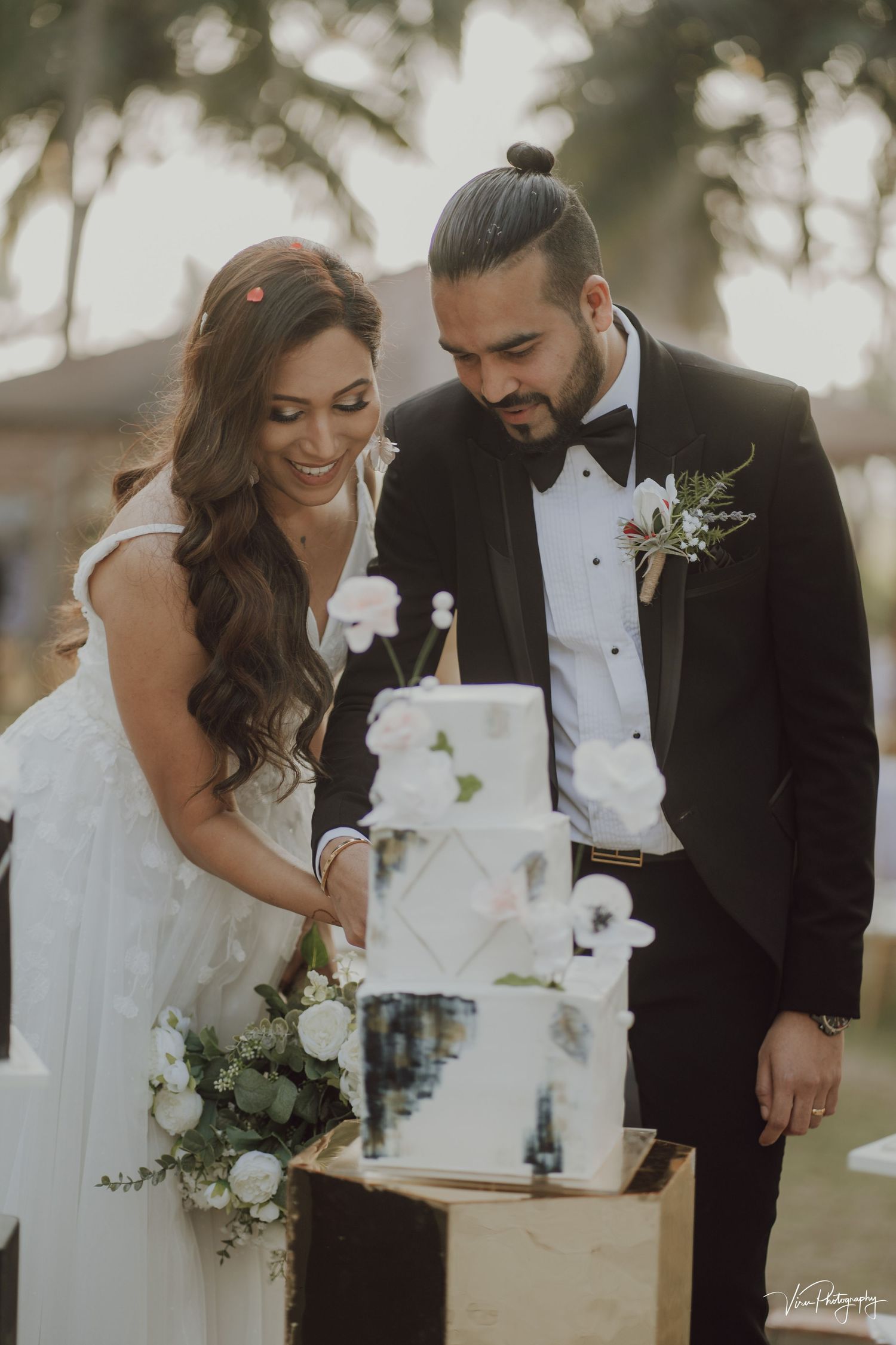 A romantic wedding moment as newlyweds prepare to cut into their elegant white tiered cake during a dreamy golden hour celebration.