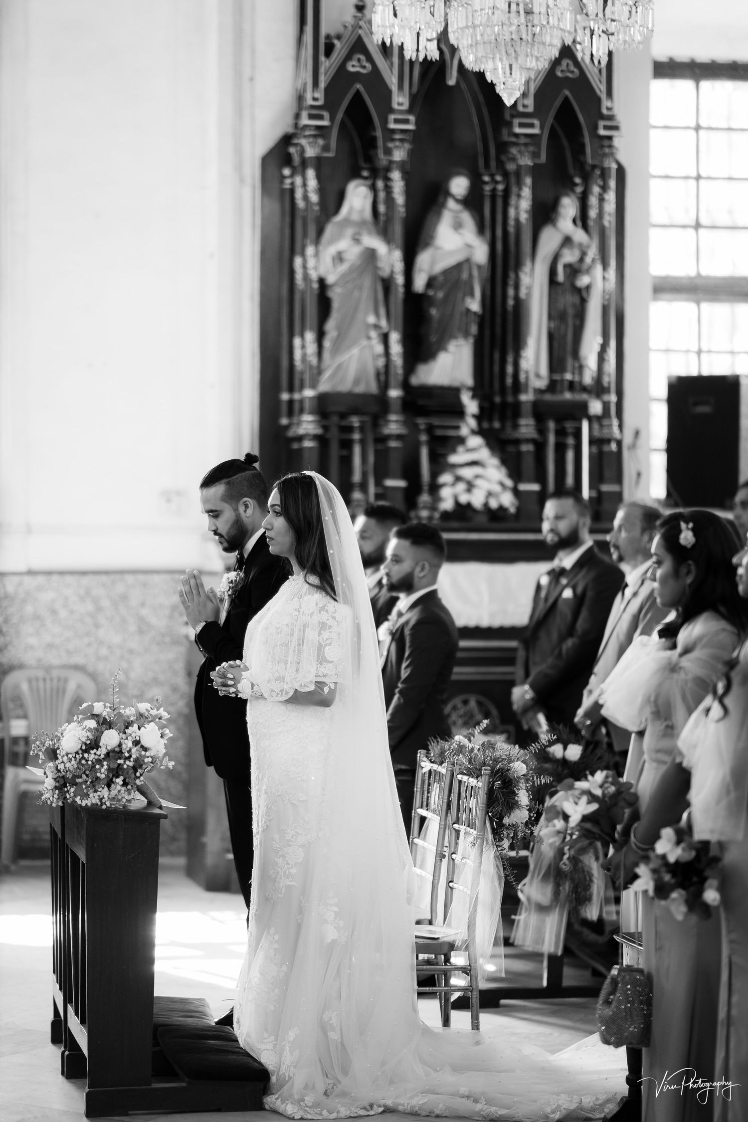 Black and white photo of a couple at their church wedding ceremony with ornate gothic archways and religious statues in background.