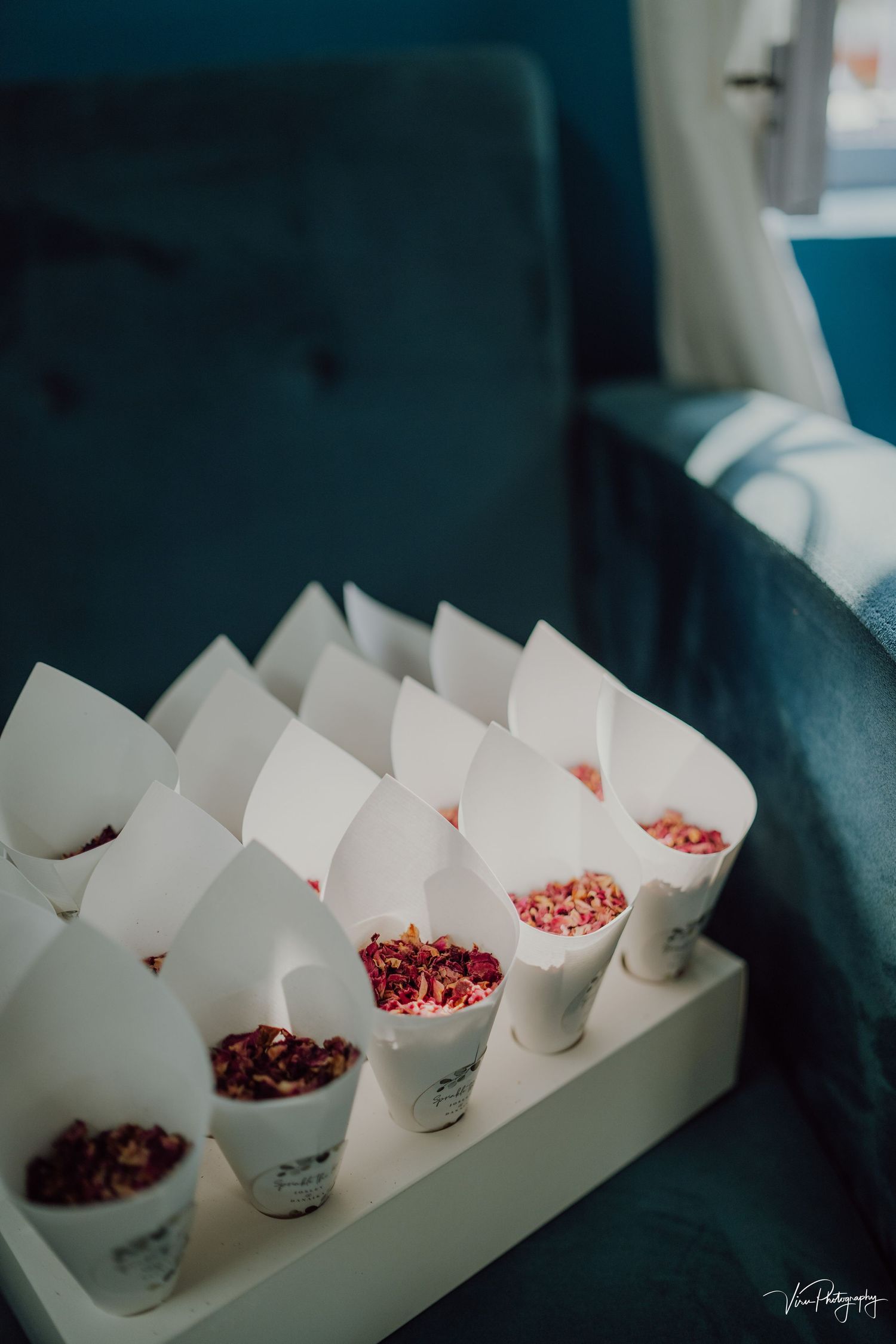 White paper cones filled with dried red petals or confetti arranged neatly in a tray for an event or celebration.