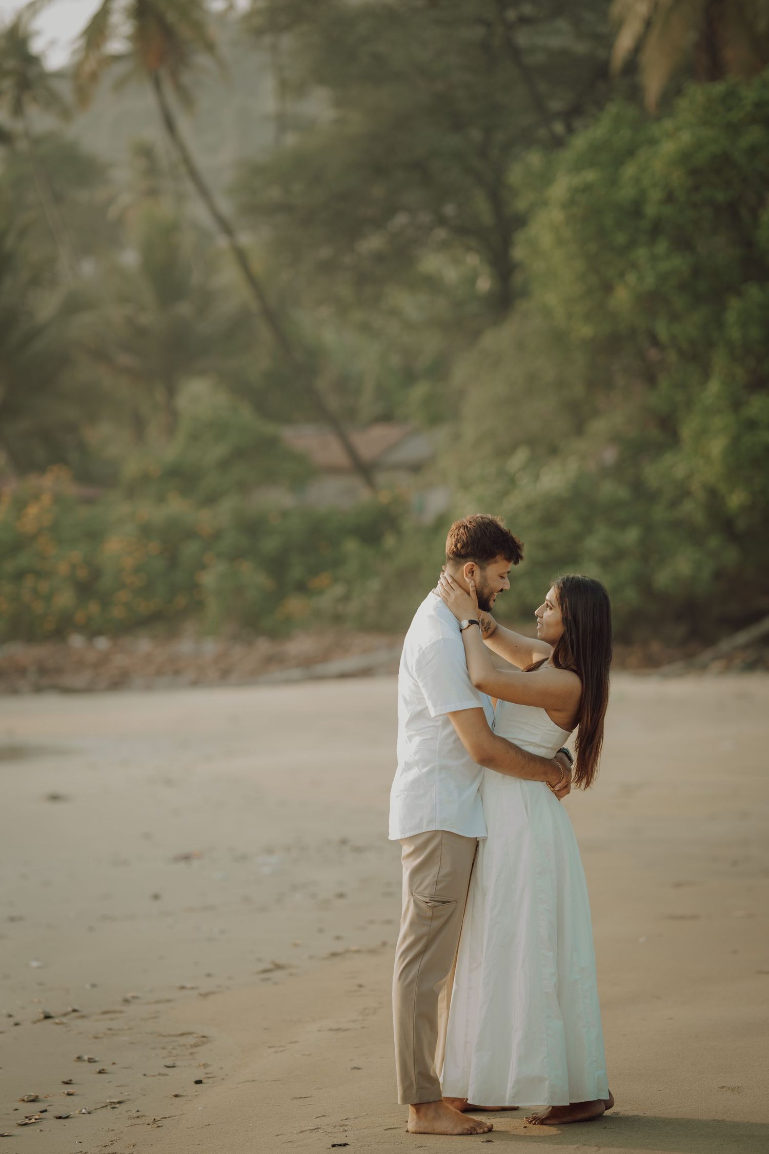 A romantic couple shares an intimate moment on a misty beach in white attire.