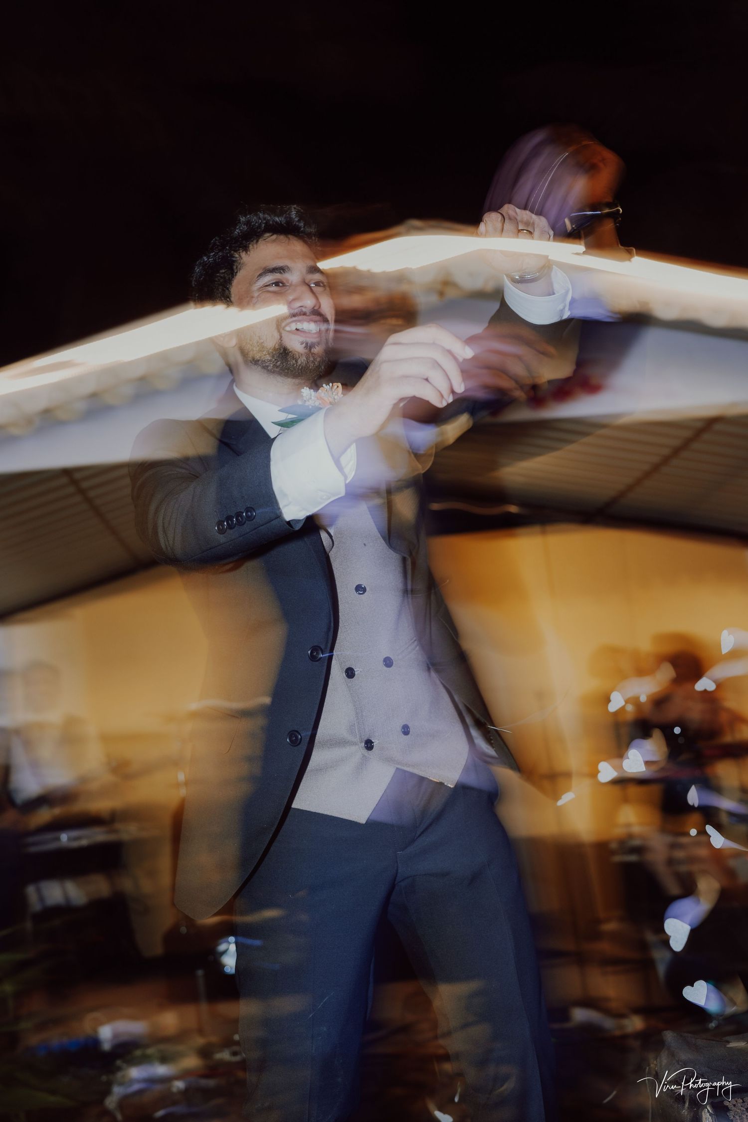 A person in a suit dances energetically at an event, captured with motion blur effect in warm lighting.