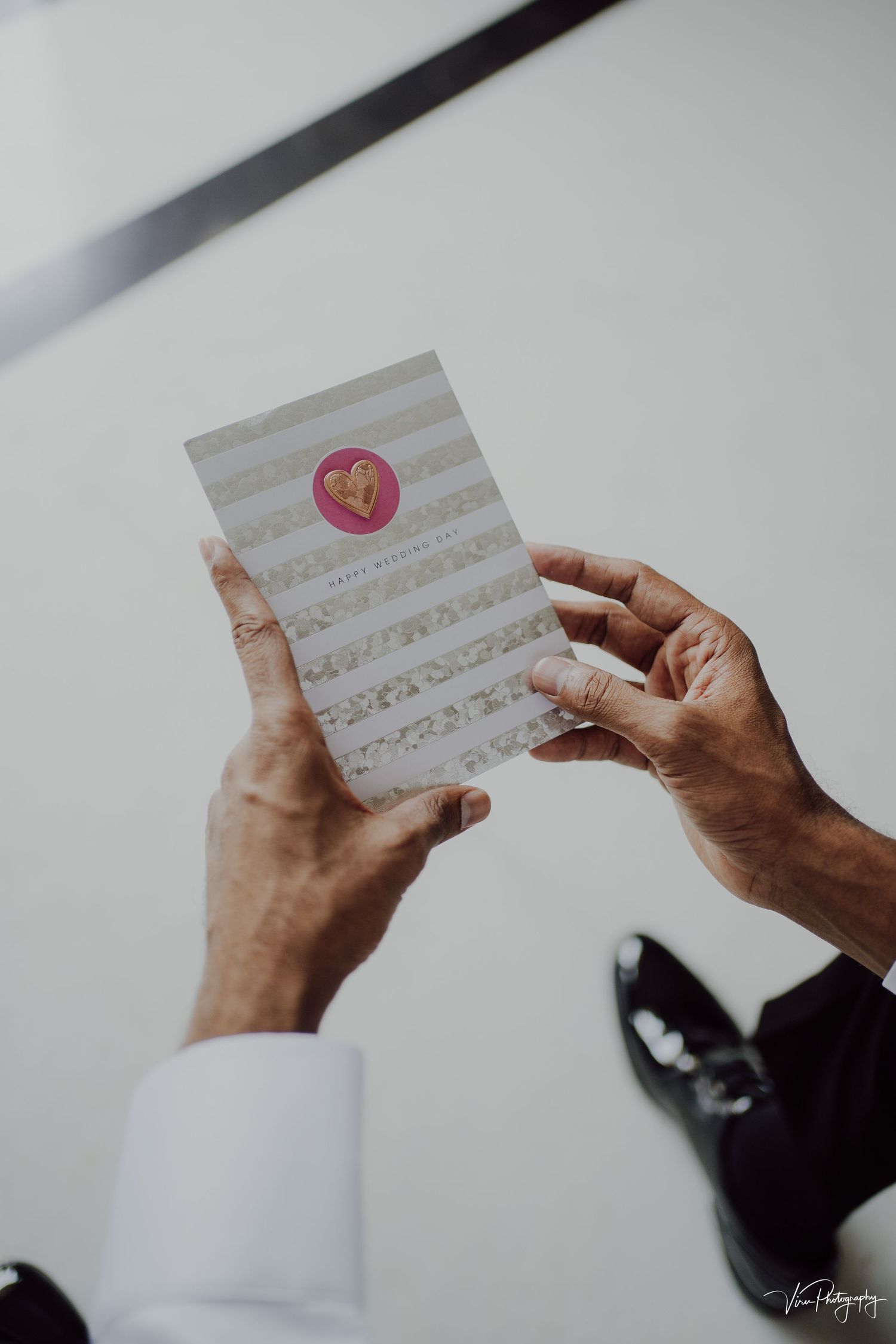 Hands holding a light colored greeting card with a pink heart seal on a white background.