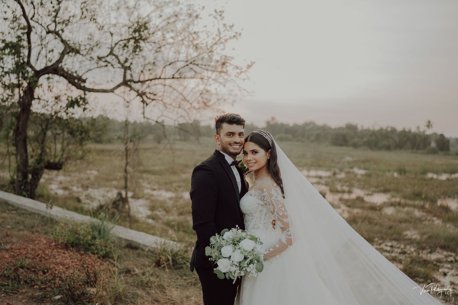 A romantic outdoor wedding photo shows a couple embracing in the countryside with a foggy landscape behind them.