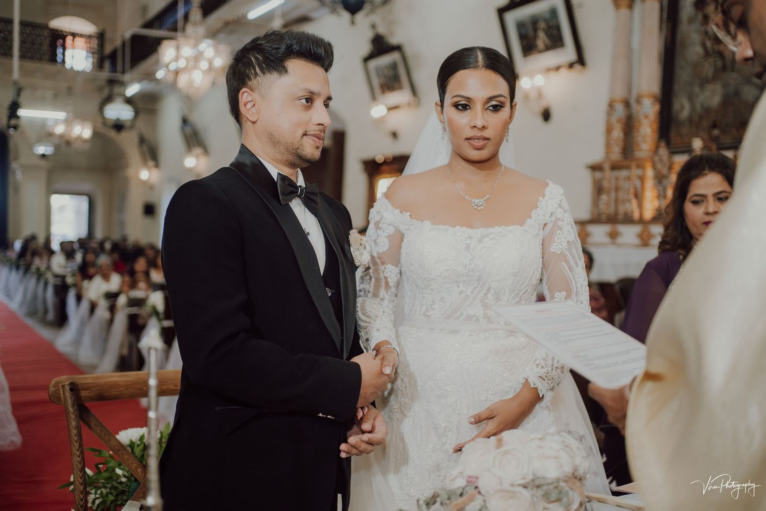 Couple stands at the altar during their traditional church wedding ceremony wearing formal black and white attire.
