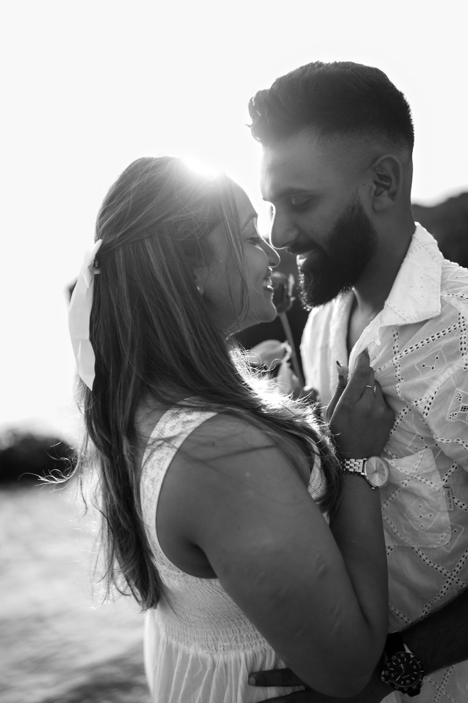 A romantic black and white photo series showing a couple embracing and kissing on the beach at sunset.