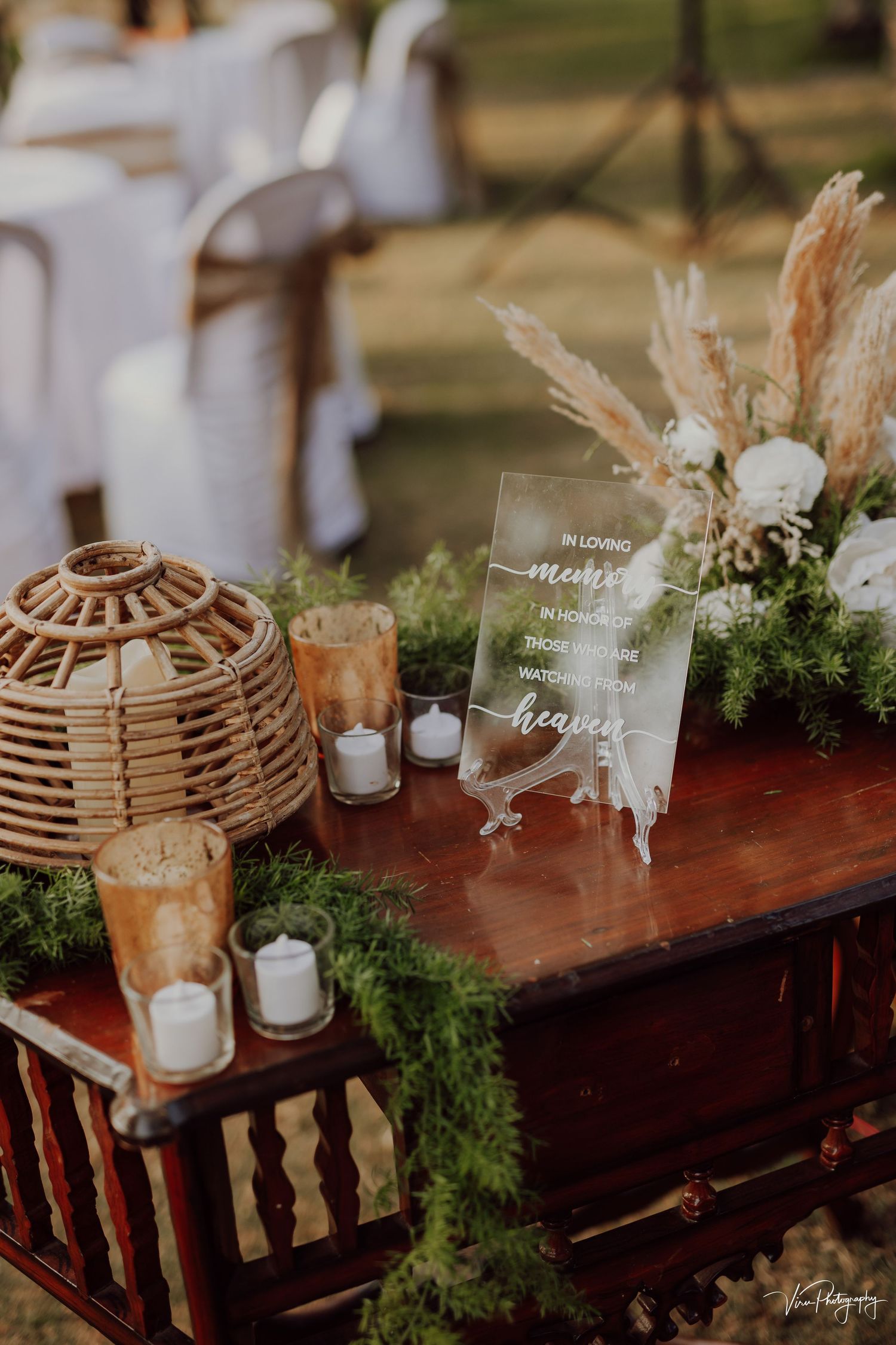 Rustic wedding decor featuring a bamboo lantern, clear acrylic signage, and pampas grass arrangements on a wooden table.