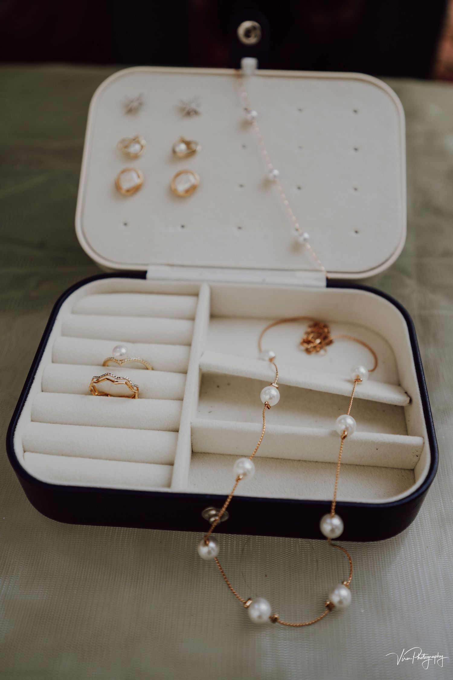Elegant pearl and gold jewelry displayed in an open navy jewelry box with velvet ring holders and compartments.