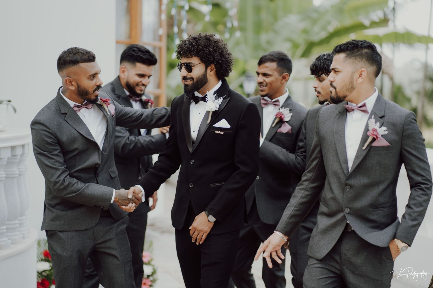 A groom and groomsmen share a candid laughing moment together while wearing formal suits on a wedding day.