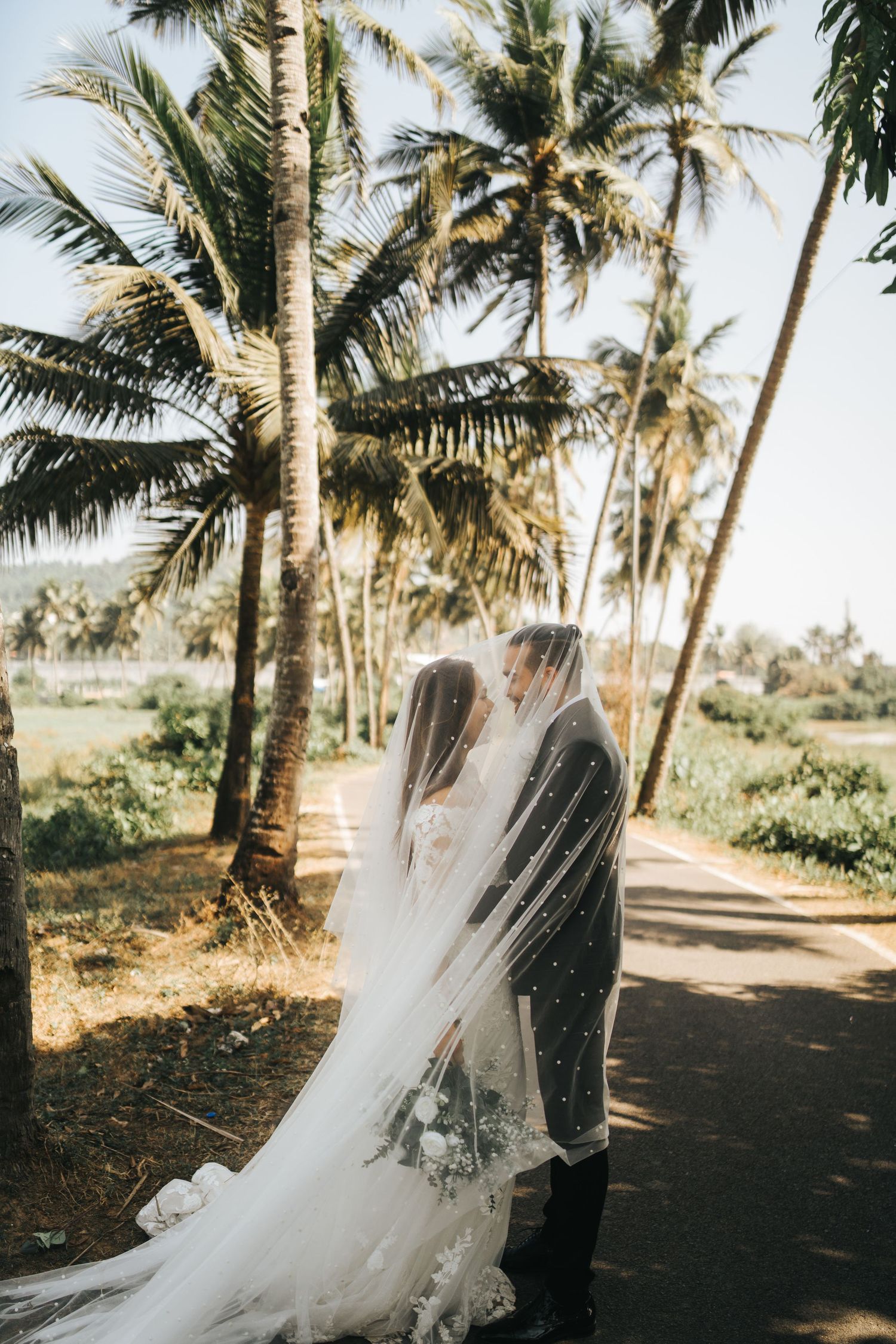 A couple embraces under tall palm trees on a scenic tropical path during a wedding photoshoot.