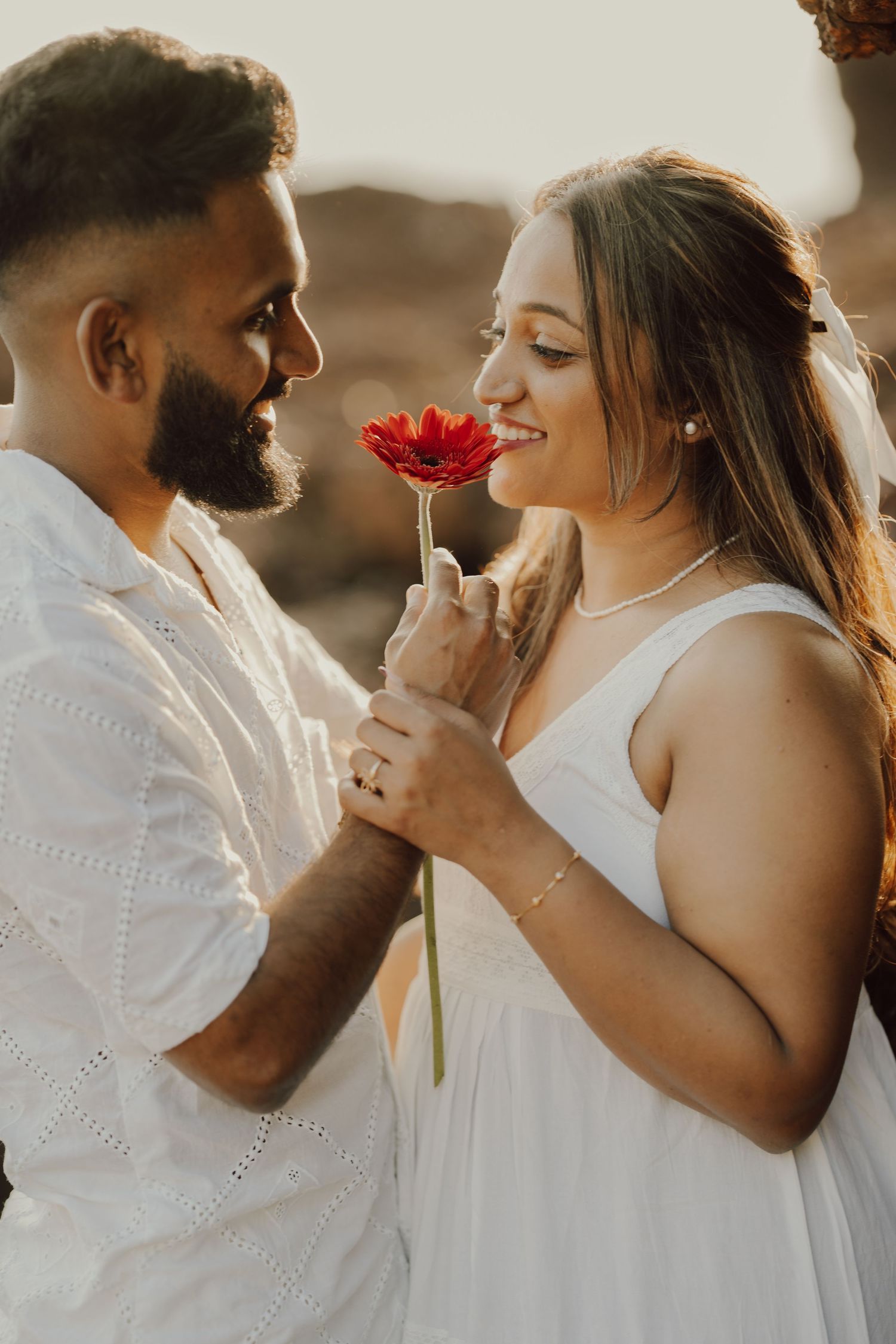 A romantic couple in white outfits share intimate moments while holding a red flower in a series of candid photos.