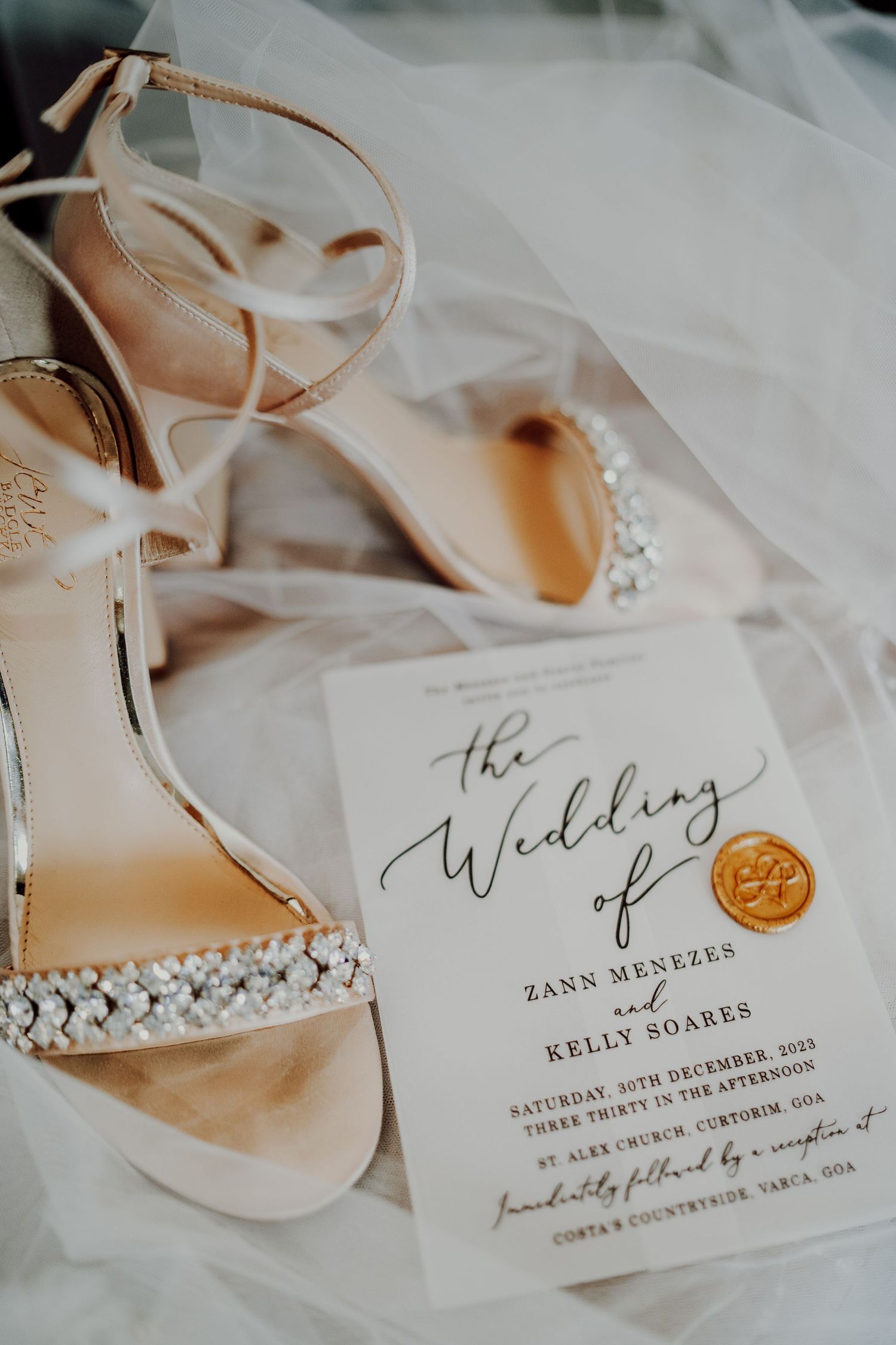 Crystal-embellished bridal sandals and wedding invitation with gold wax seal on white tulle fabric.