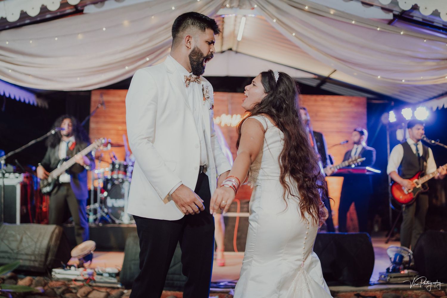 A couple shares their first dance at an evening reception with musicians performing on stage in the background.