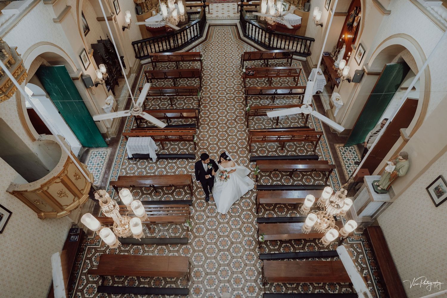 Aerial view of a grand staircase in an elegant venue with ornate carpet and two figures standing on the landing.
