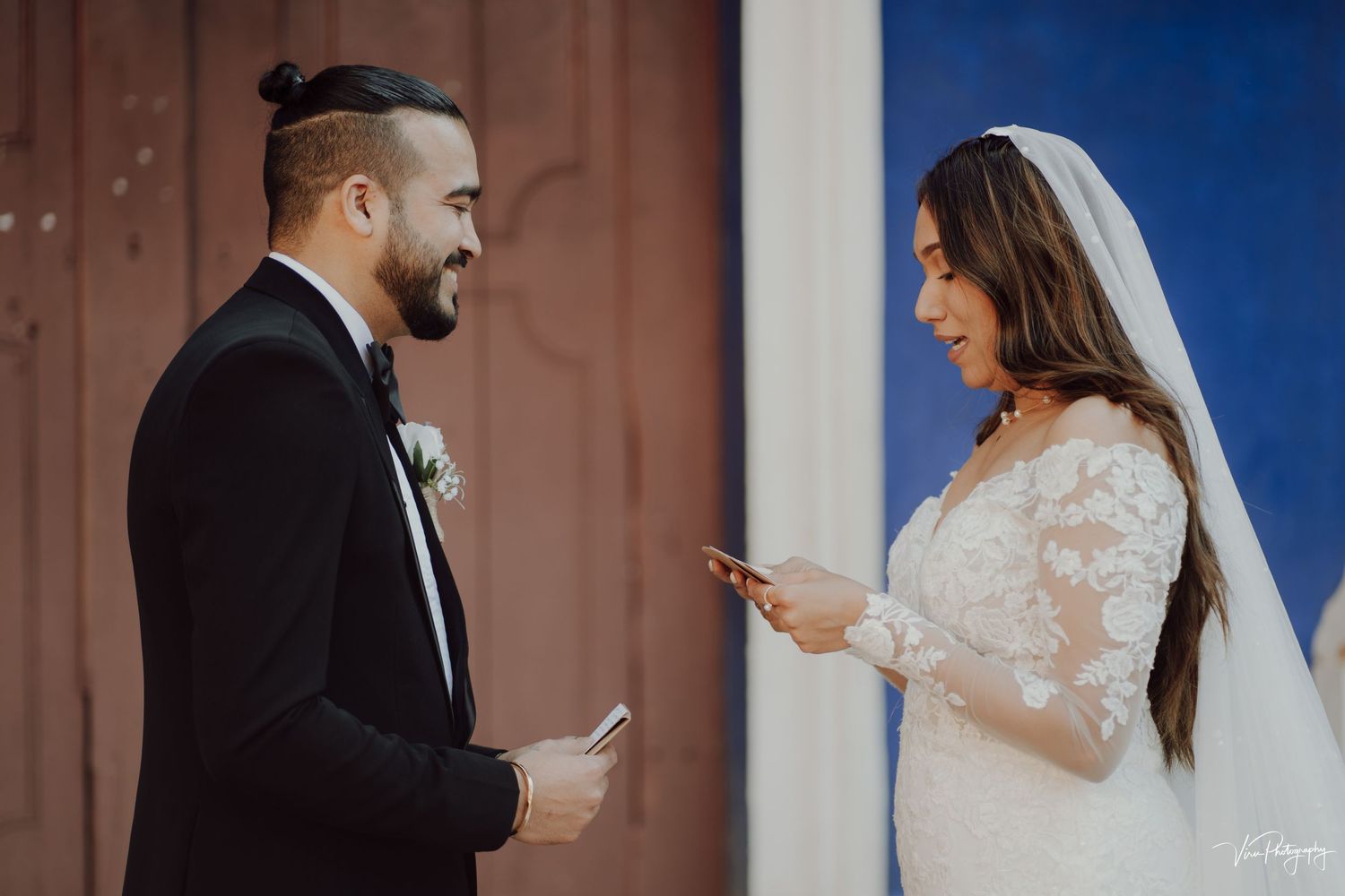 Bride and groom sharing a moment while reading vows to each other outside against a blue sky.
