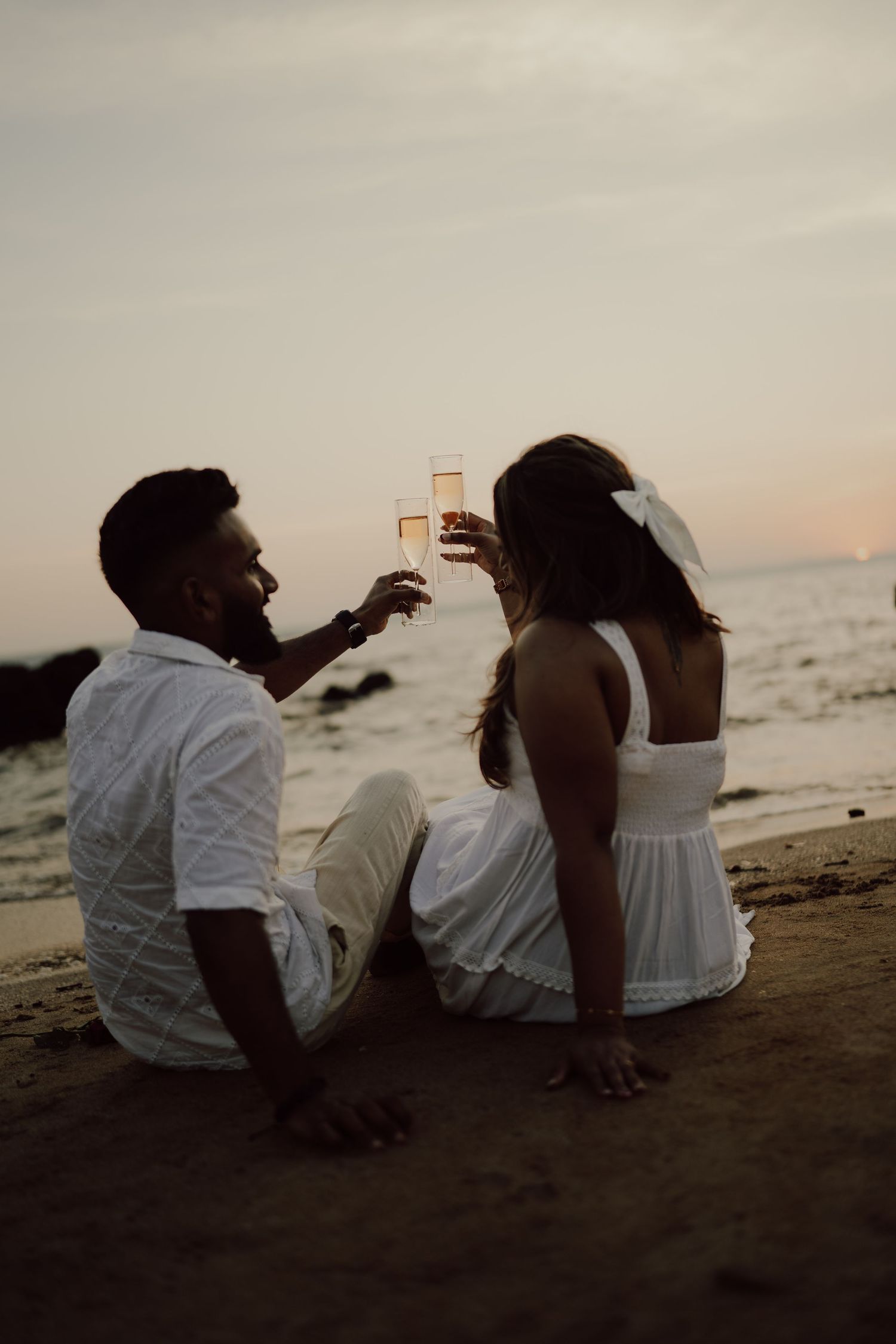 A couple sits together on the beach at sunset sharing drinks and enjoying the peaceful ocean view.