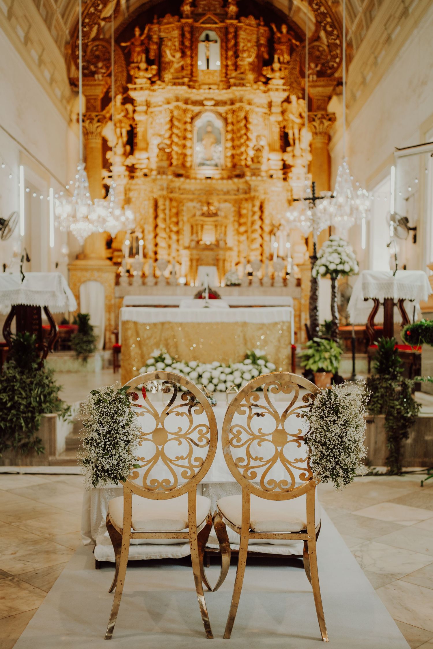 Ornate golden church altar decorated with white flowers and elegant chairs for a wedding ceremony.