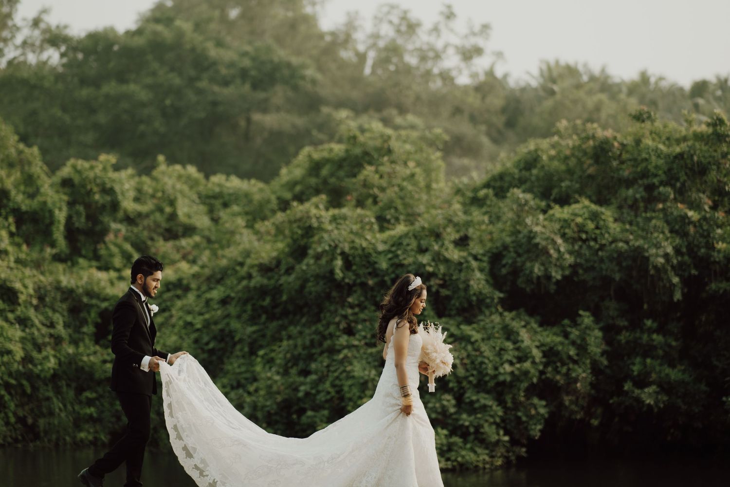 Wedding couple in garden setting with bride's long white veil flowing in the breeze.