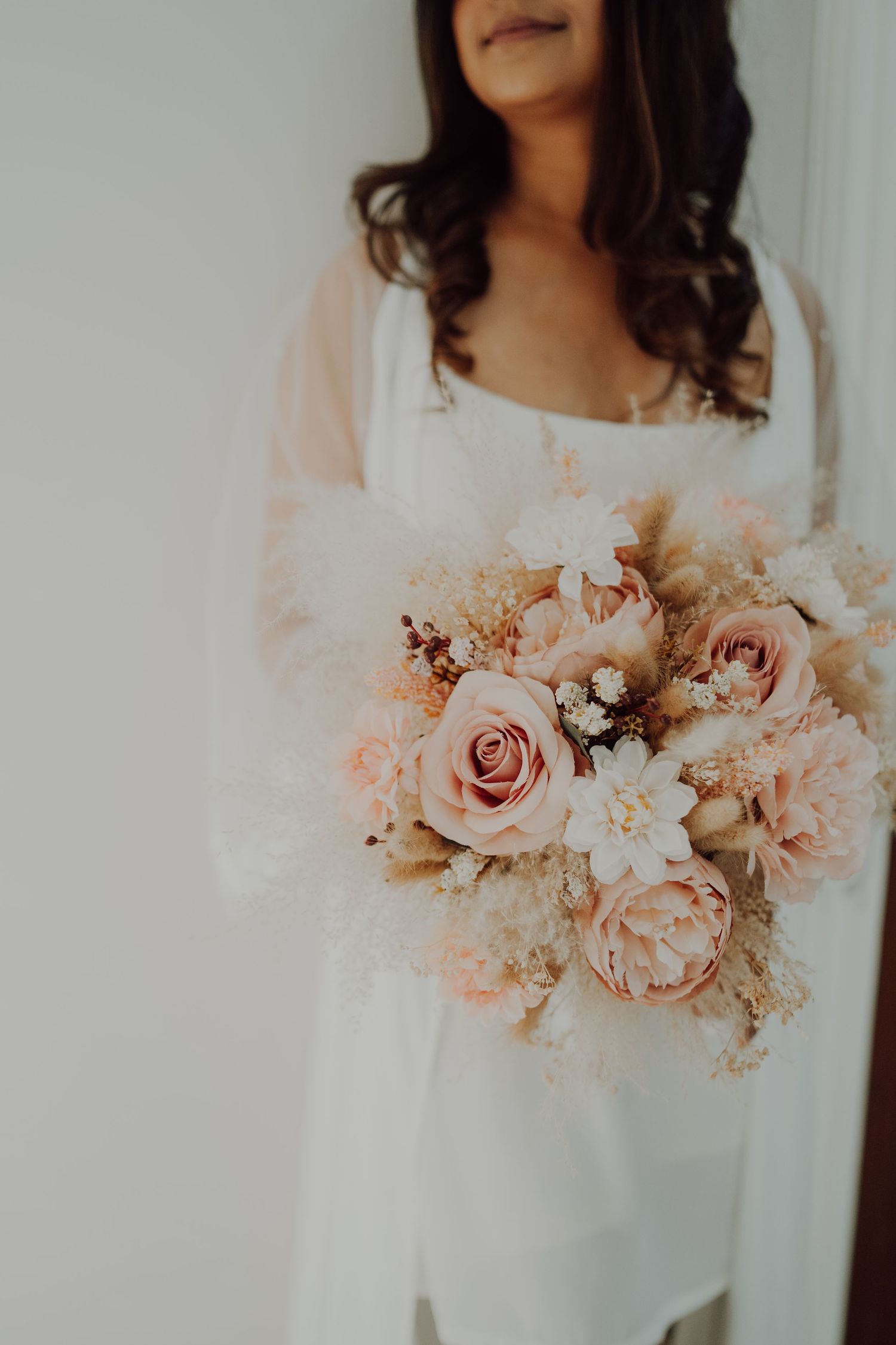 Soft pink and white wedding bouquet held against a white bridal gown.
