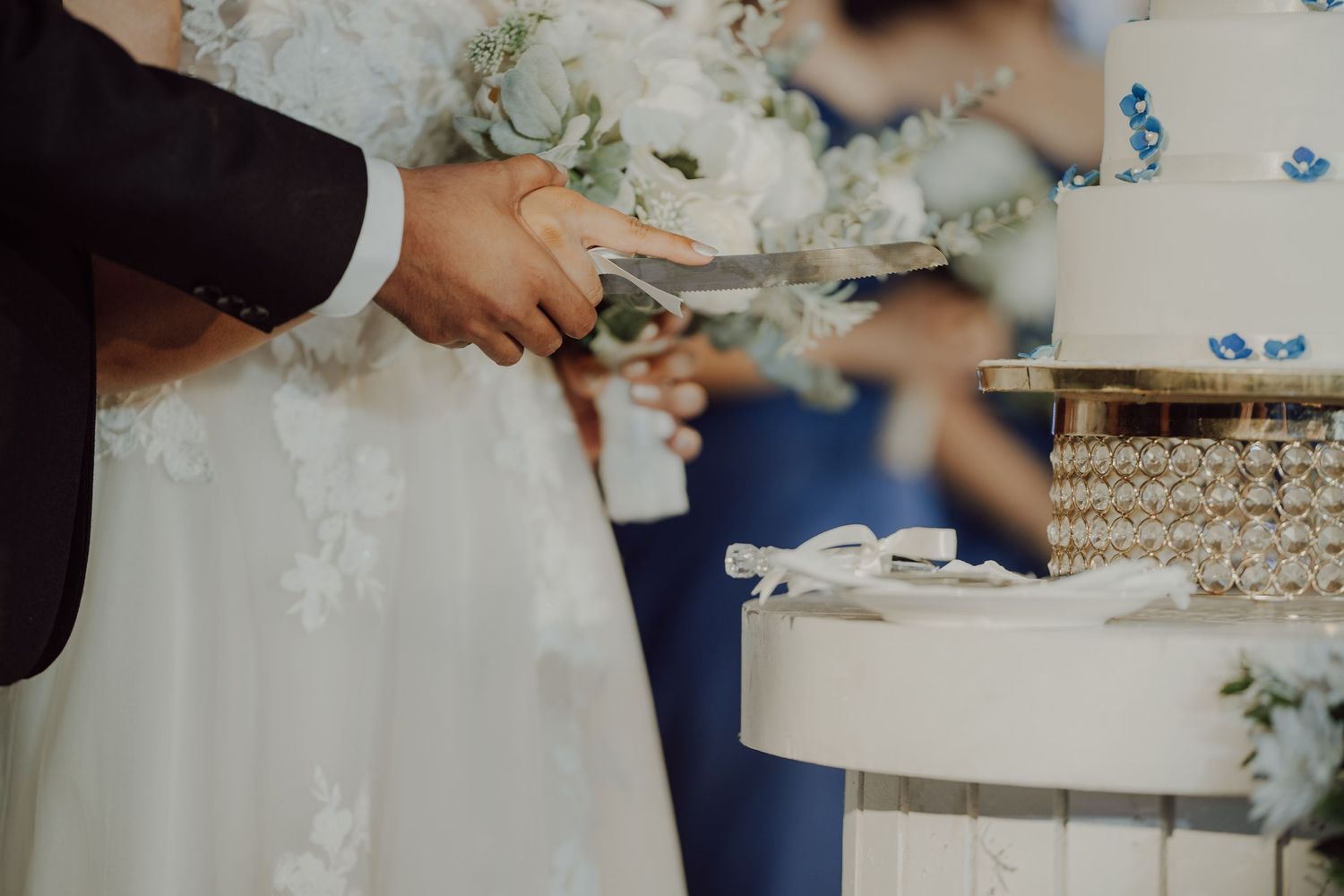 Hands cutting into an elegant white wedding cake with floral decorations.
