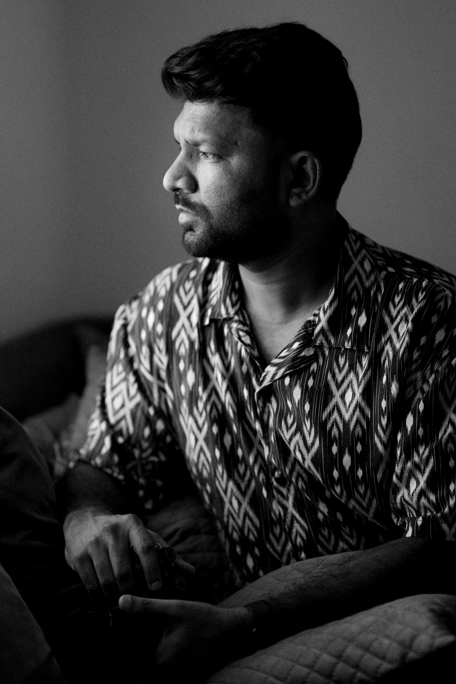 Black and white portrait of a contemplative person in a patterned shirt looking to the side in dramatic lighting.