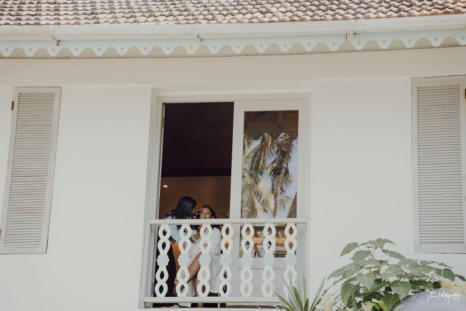 A white balcony with ornate railing and shutters on the windows of a colonial style building.