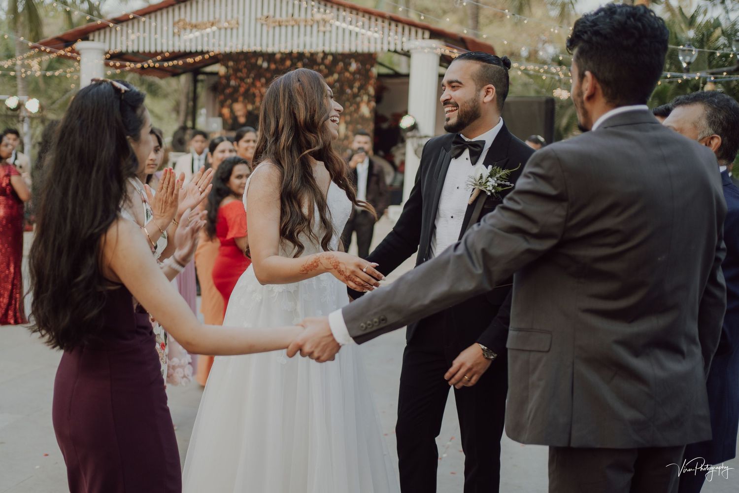 Wedding guests congratulate the newlyweds with hugs and handshakes at an outdoor reception venue.