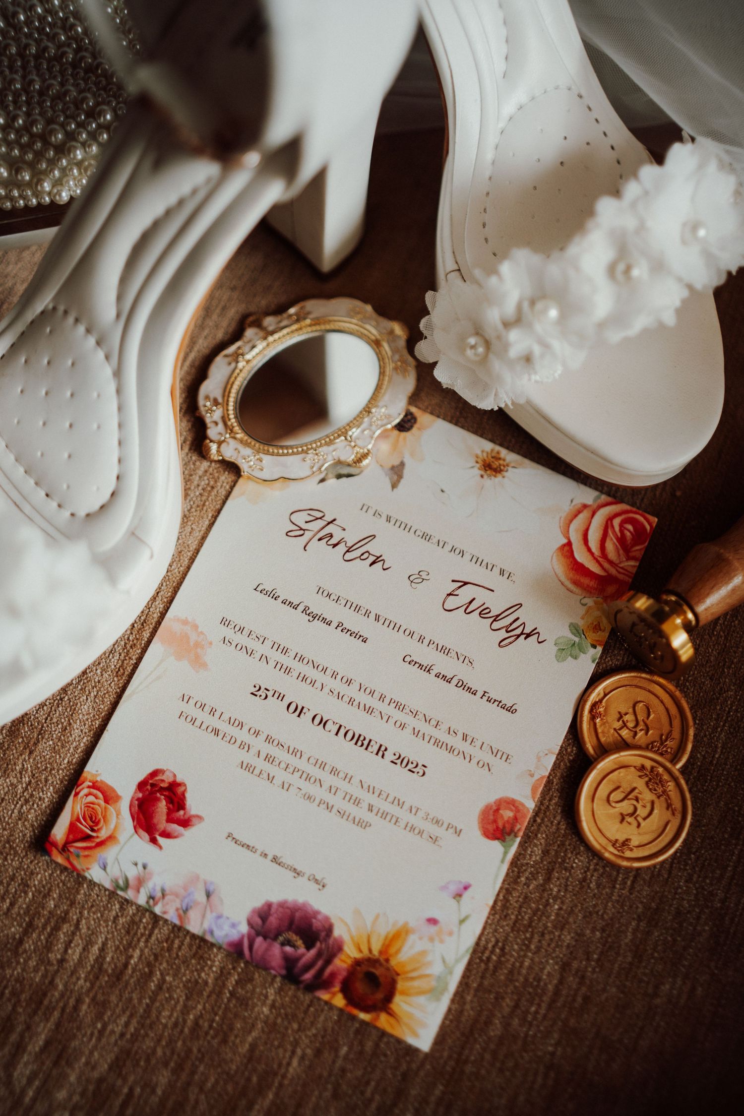 Floral wedding invitation with wax seals, a vintage mirror and white platform bridal heels with flower details on a woven backdrop.