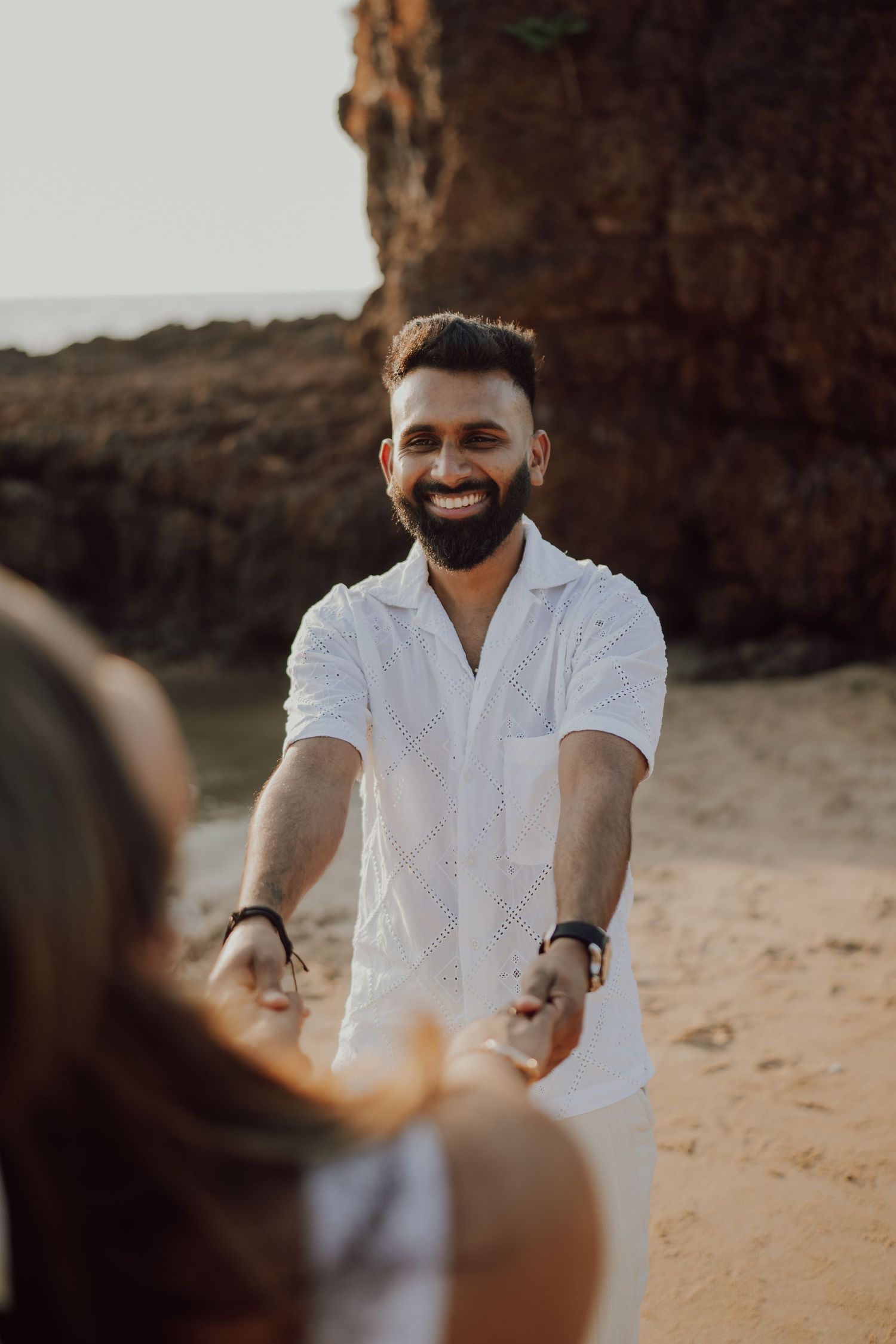 A person in a white shirt stands on a sandy beach at sunset with cliffs in the background.
