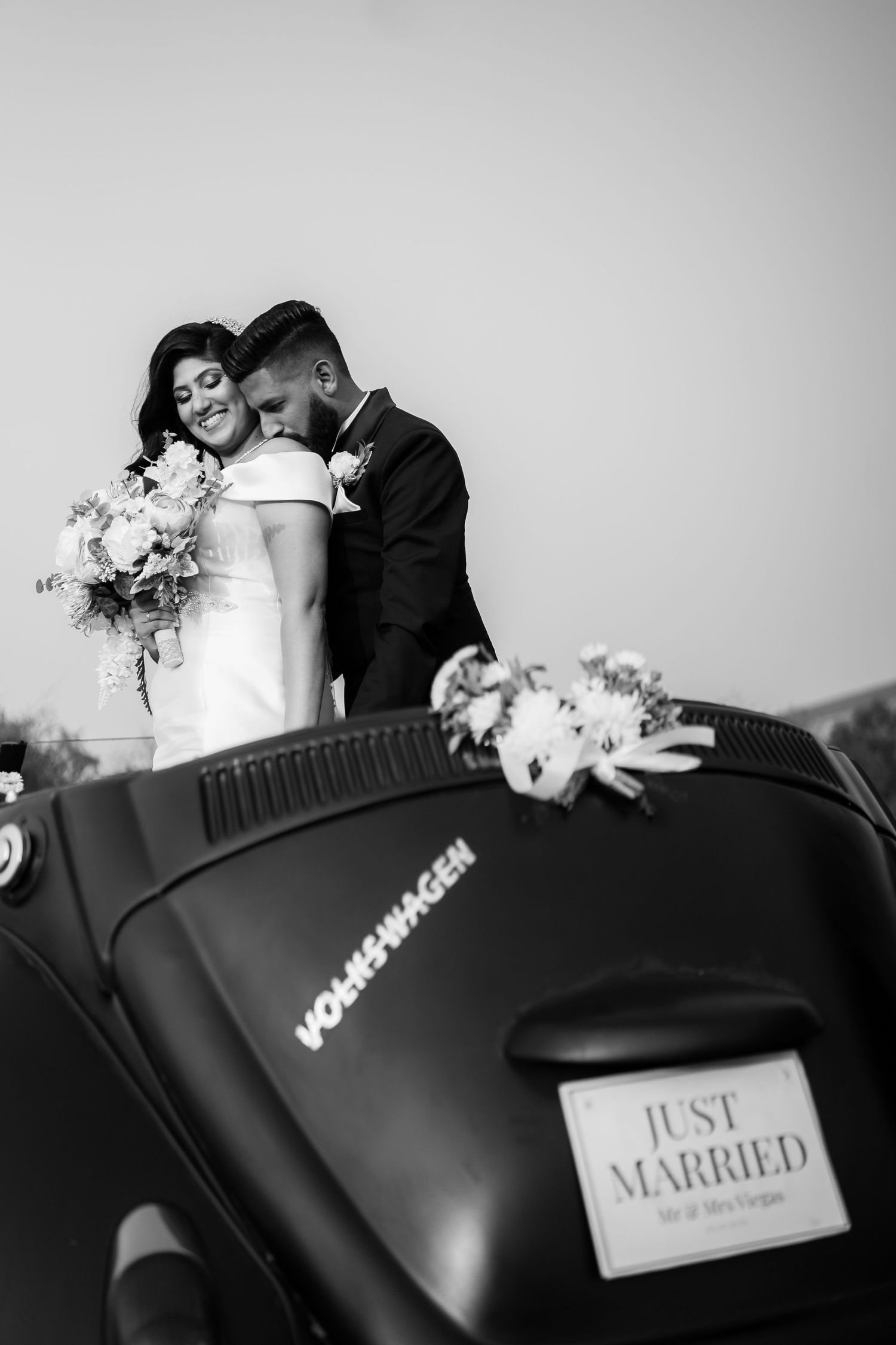 Black and white wedding photo featuring a classic VW Beetle with 'Just Married' sign and elegant floral decorations.