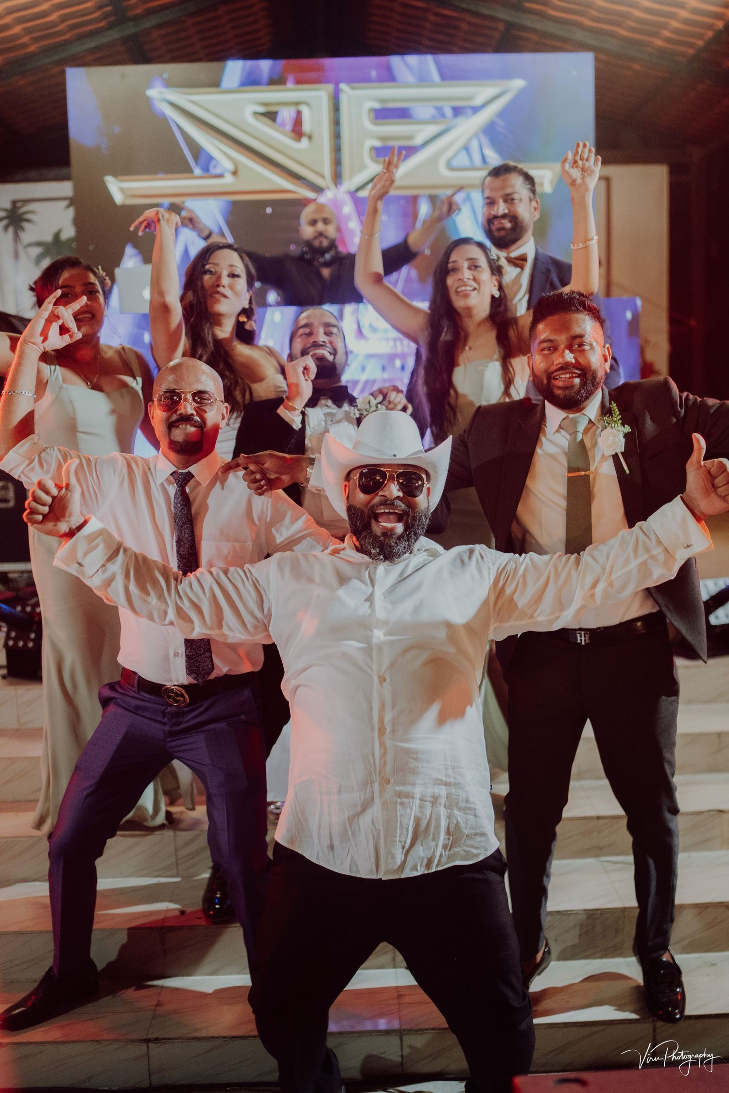 A group of people dancing and celebrating at a party with colorful lighting and music in the background.