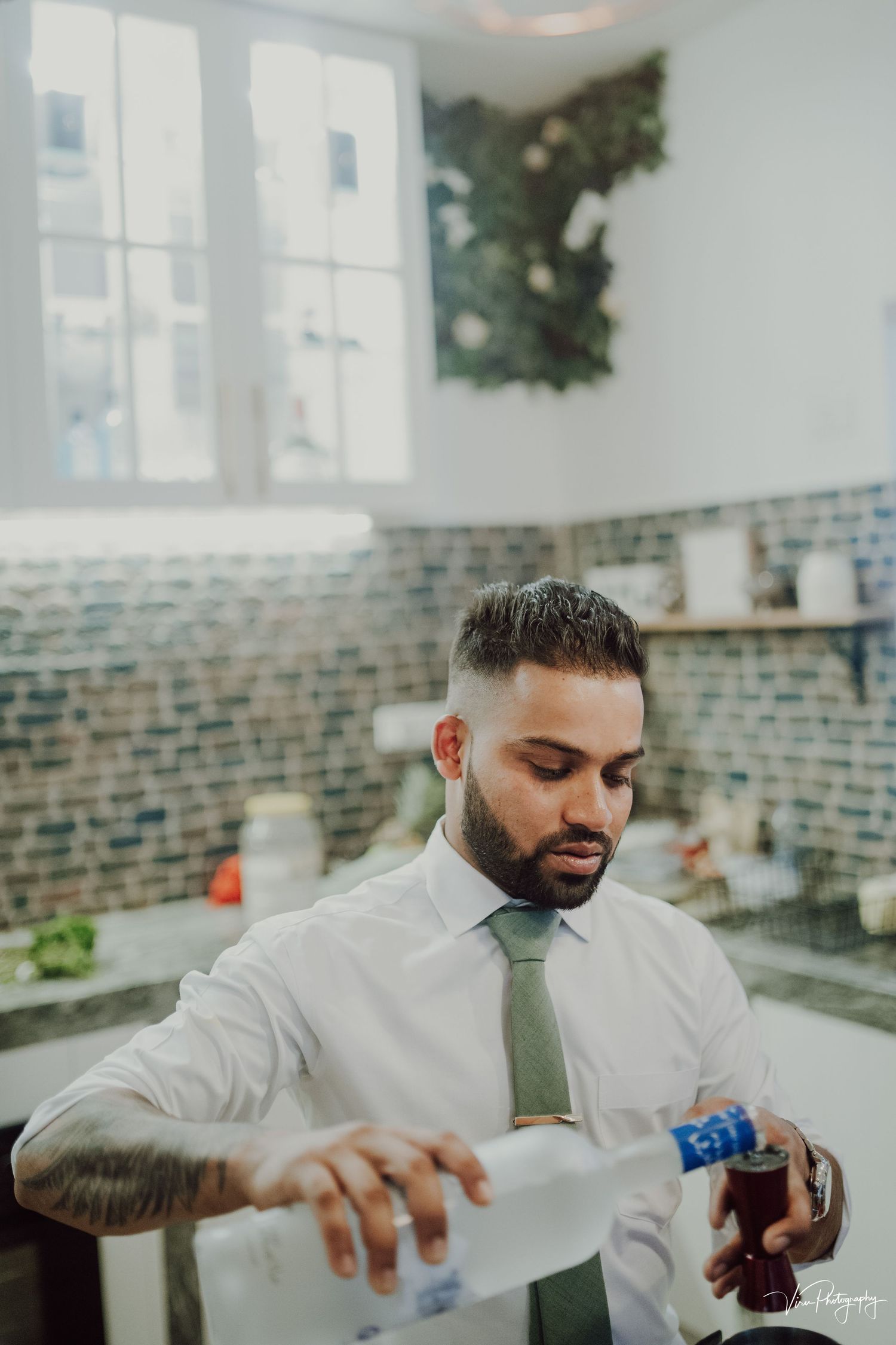 Professional bartender in white shirt and tie pours a drink while working behind a brick-walled bar area.
