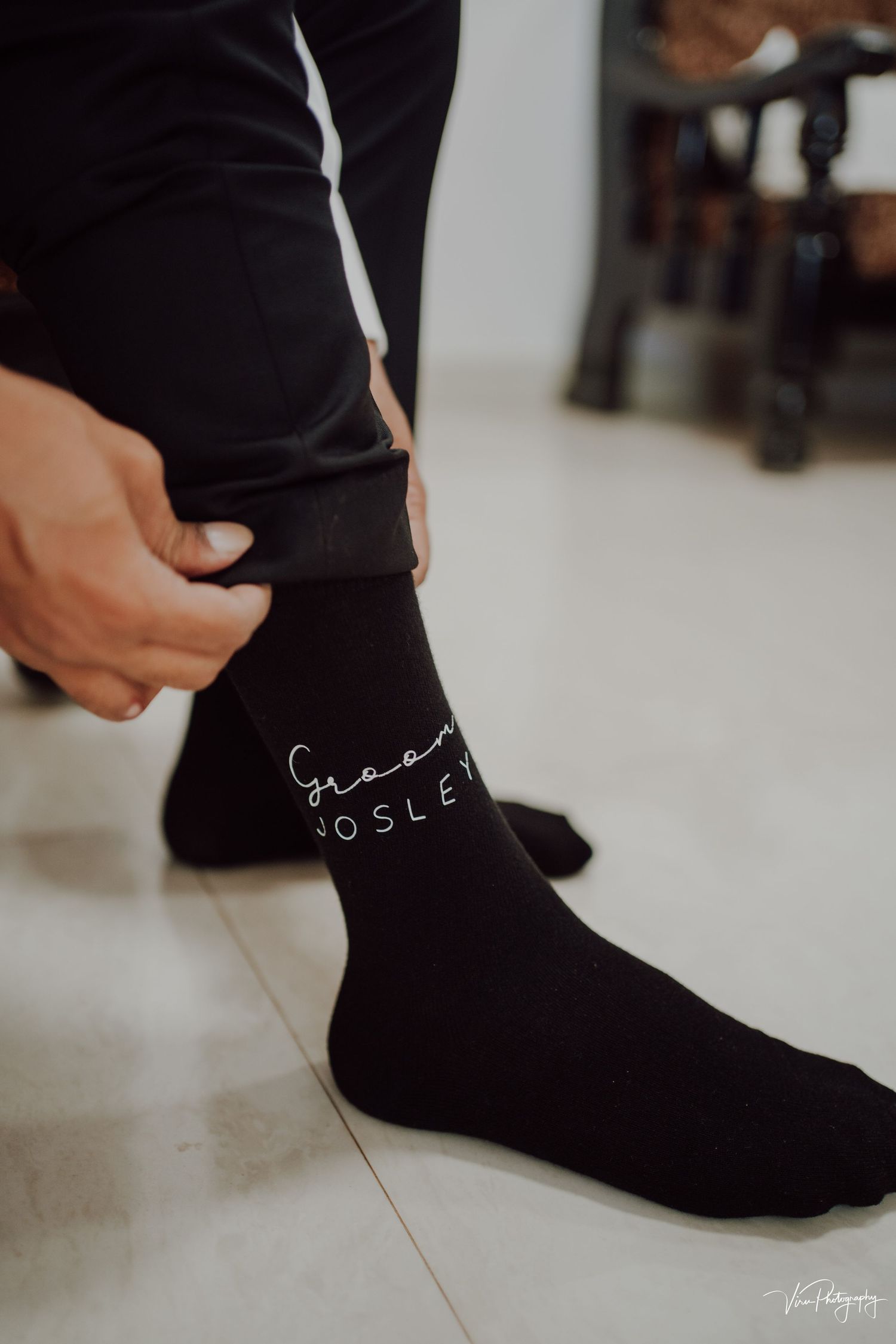 Close-up view of a person wearing black socks with white text branding on a light tile floor.