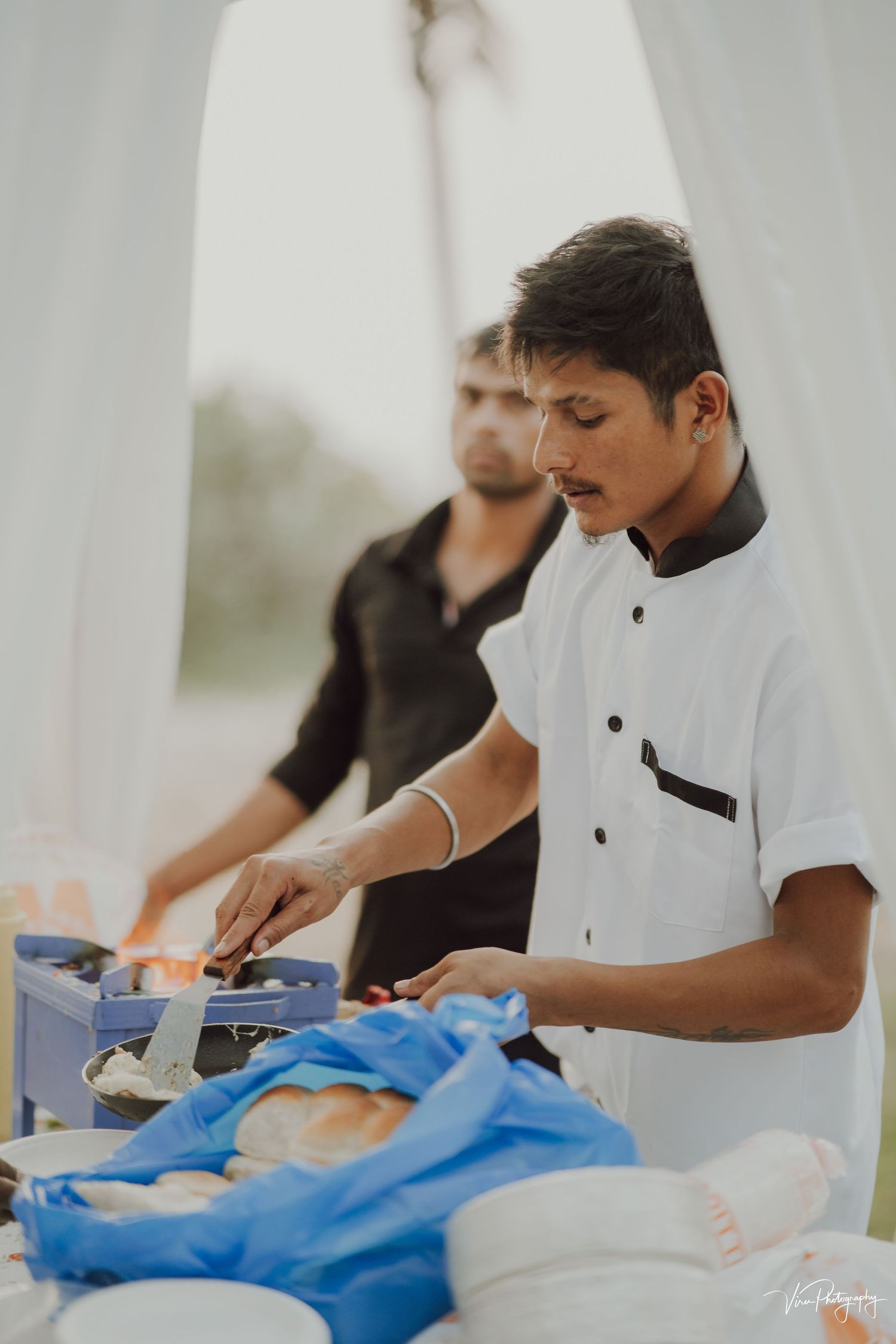 Chef in white uniform preparing food at outdoor catering station with professional equipment.