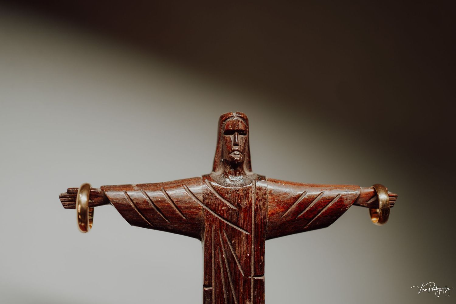 Closeup of a wooden carving statue with outstretched arms against a dark background.