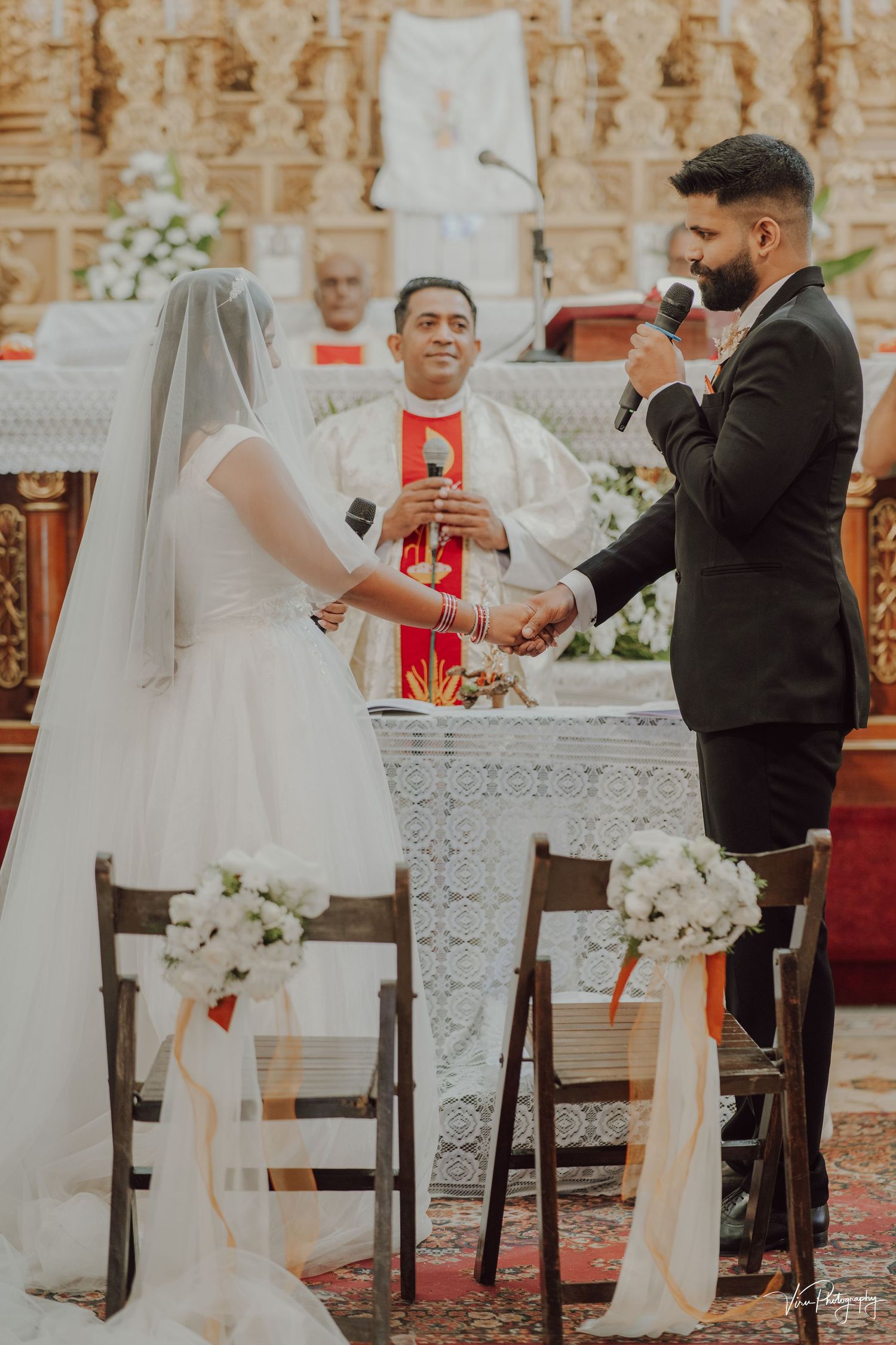 A traditional Catholic church wedding ceremony with couple exchanging vows at the altar while a priest officiates.