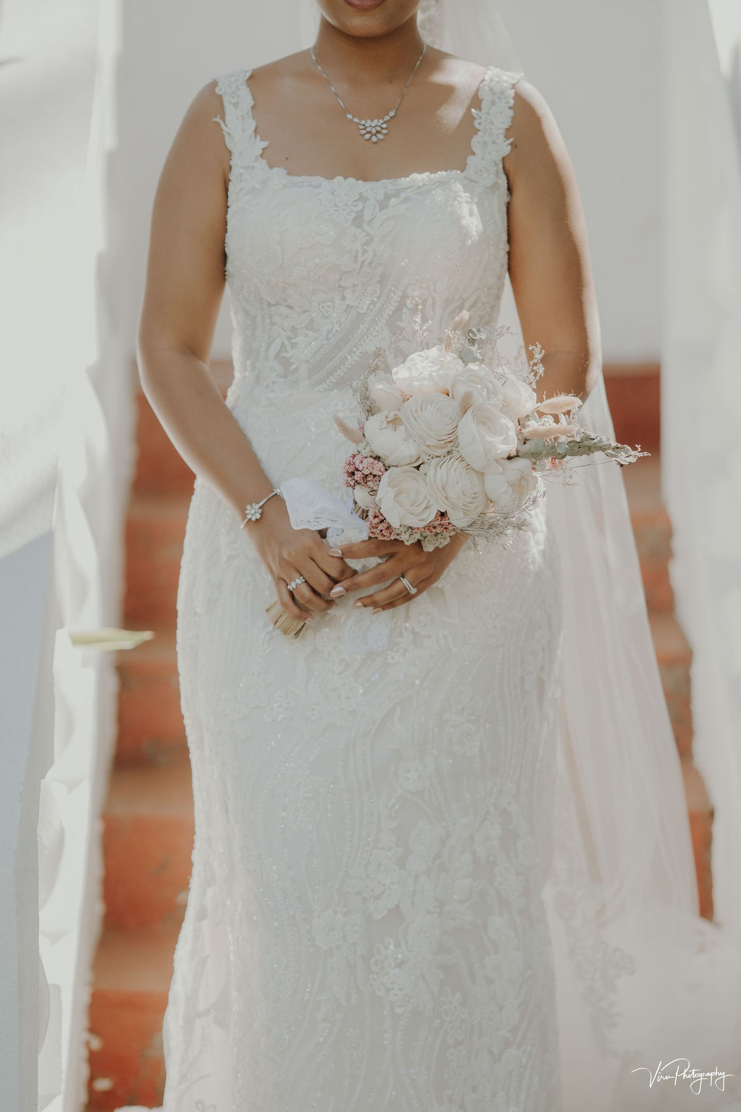 A close-up of an elegant lace wedding dress with delicate straps and a white peony bouquet.