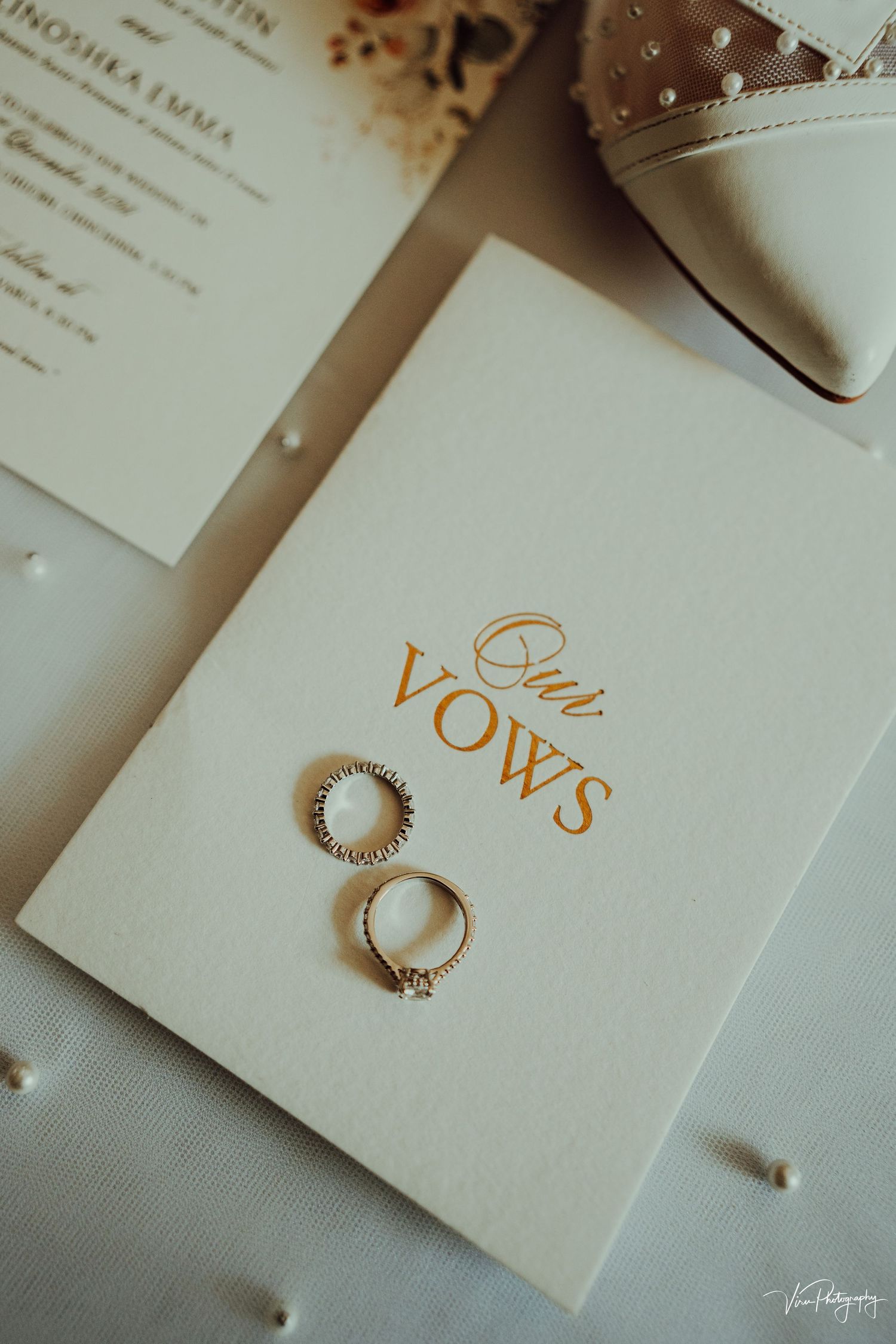 Wedding rings and vows book displayed alongside a bridal shoe in a romantic flat lay composition.