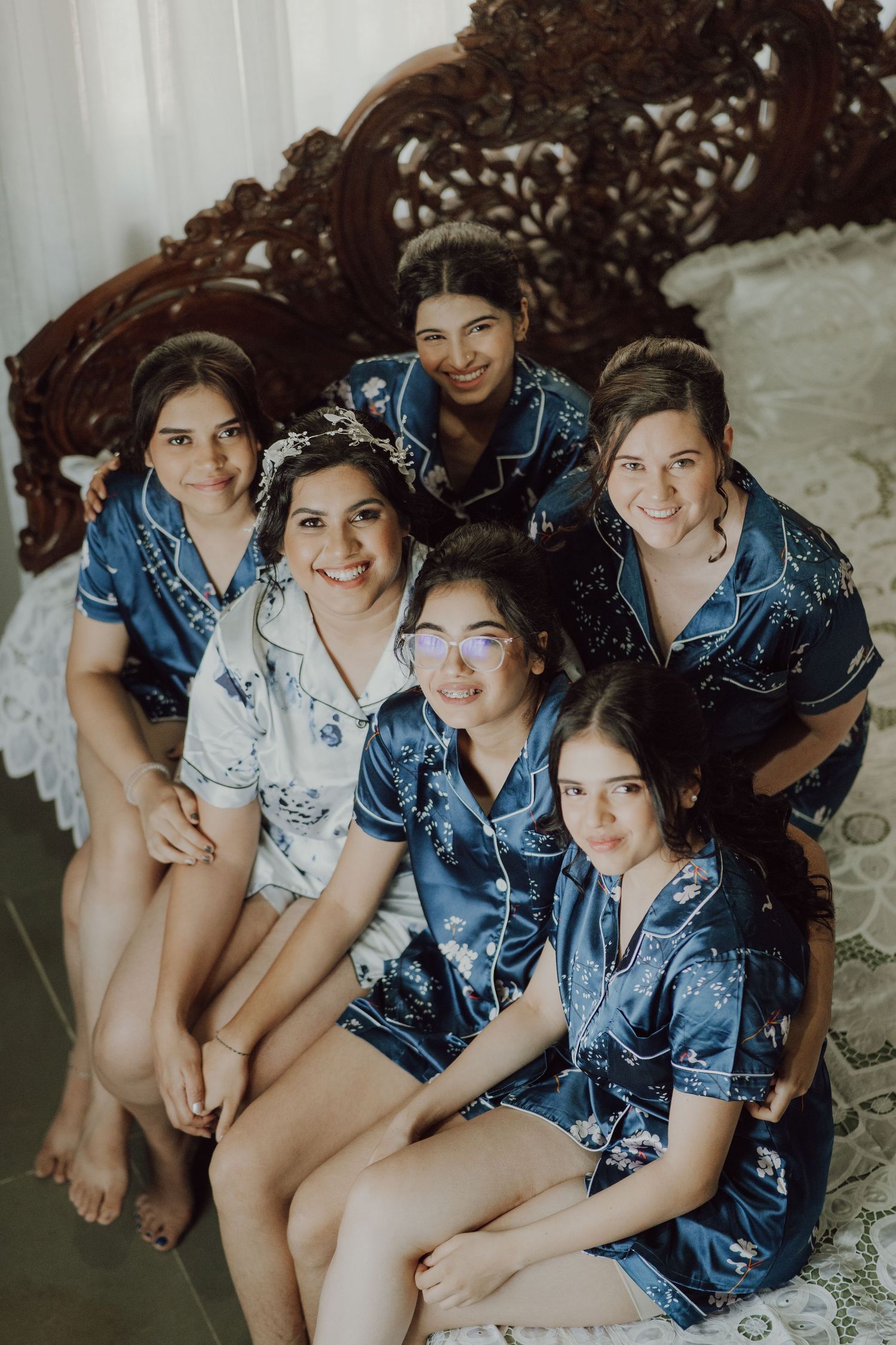 A group in matching blue satin robes pose together on an ornate bed during wedding preparations.