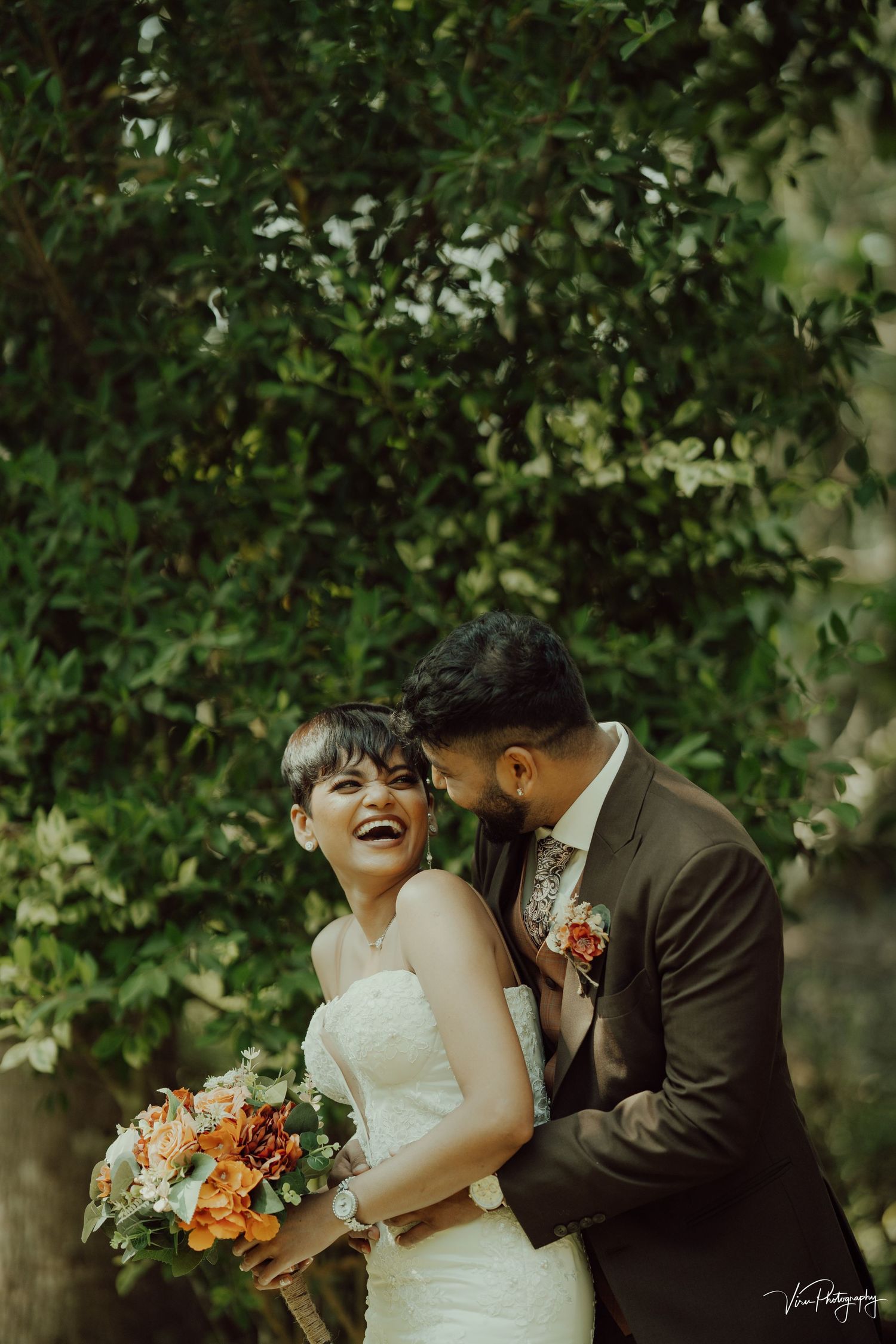 Couple embraces in an intimate moment surrounded by lush greenery during their outdoor wedding photo session.